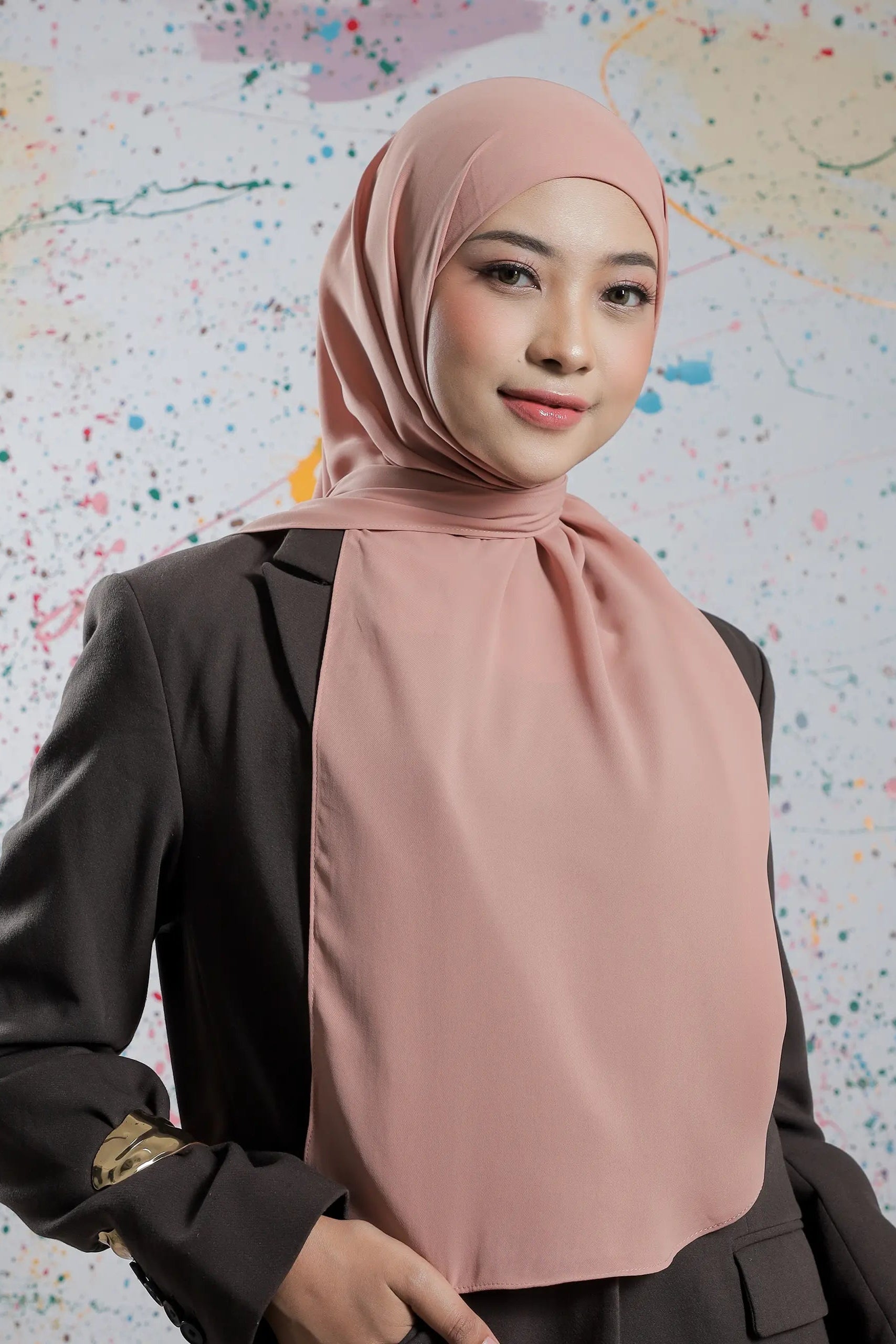 Woman wearing a pink hijab and black outfit against a colorful abstract background