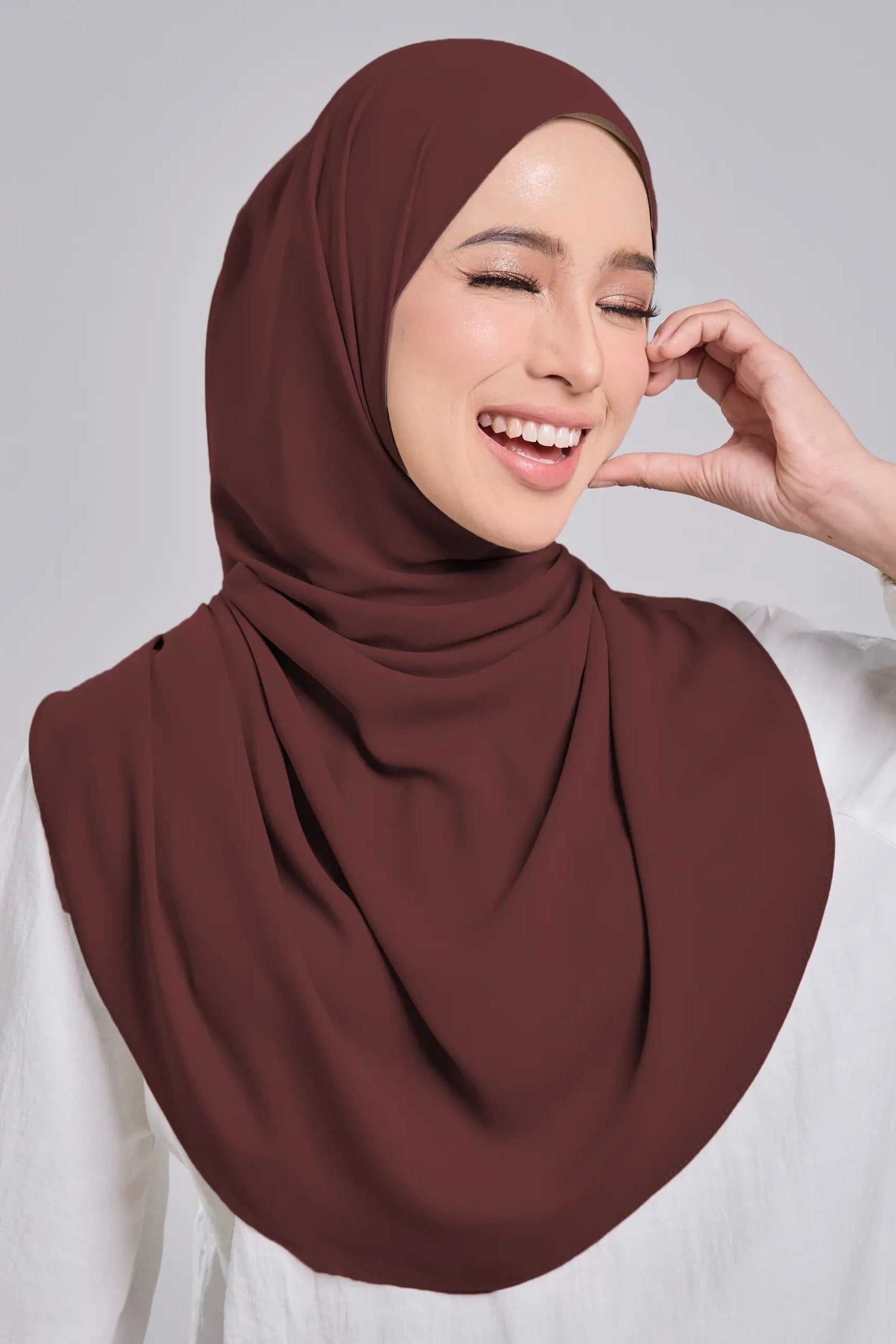 Woman wearing a brown hijab against a plain background