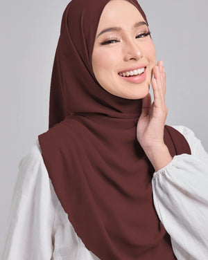 Woman wearing a brown hijab and white shirt against a gray background