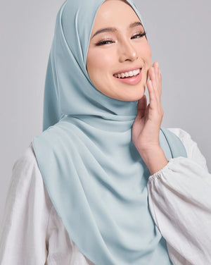 Woman wearing a light blue hijab against a gray background