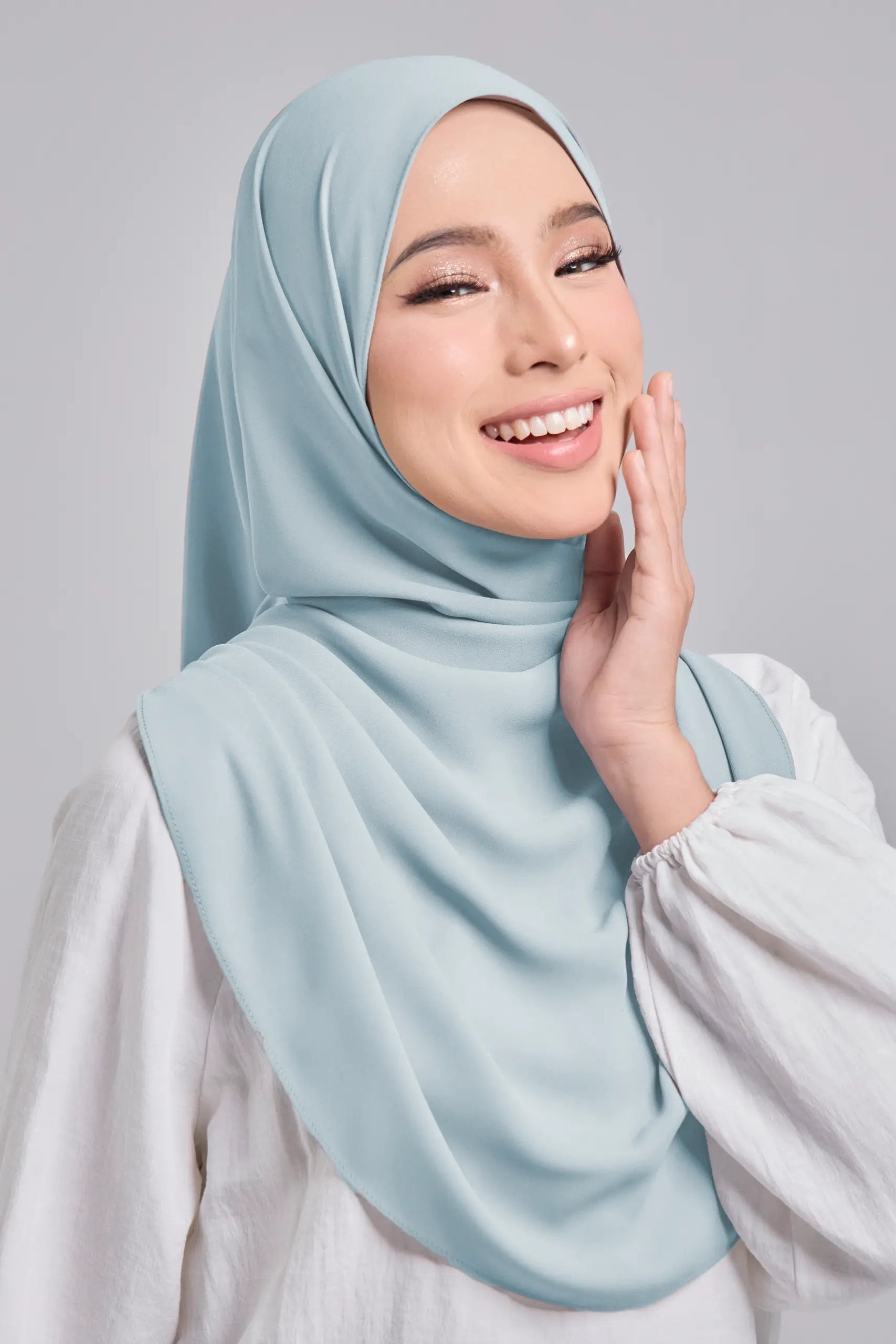 Woman wearing a light blue hijab against a gray background