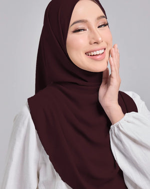 Woman wearing a brown hijab and white shirt against a gray background