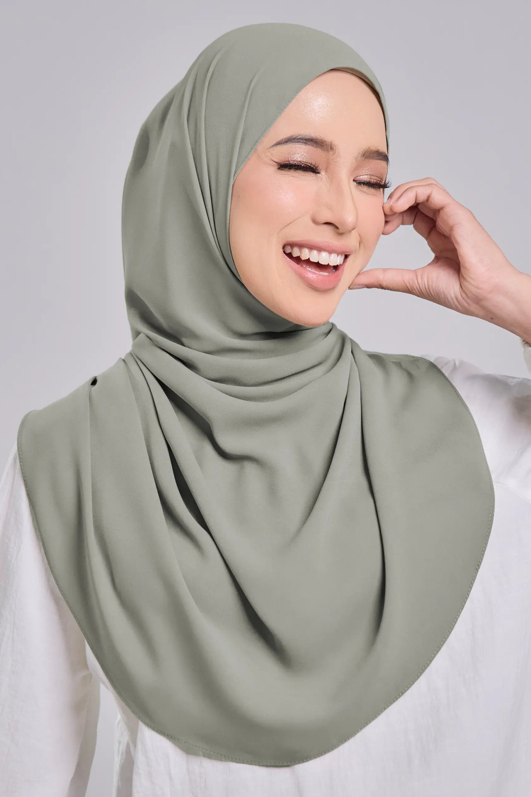 Woman wearing a light green hijab against a gray background