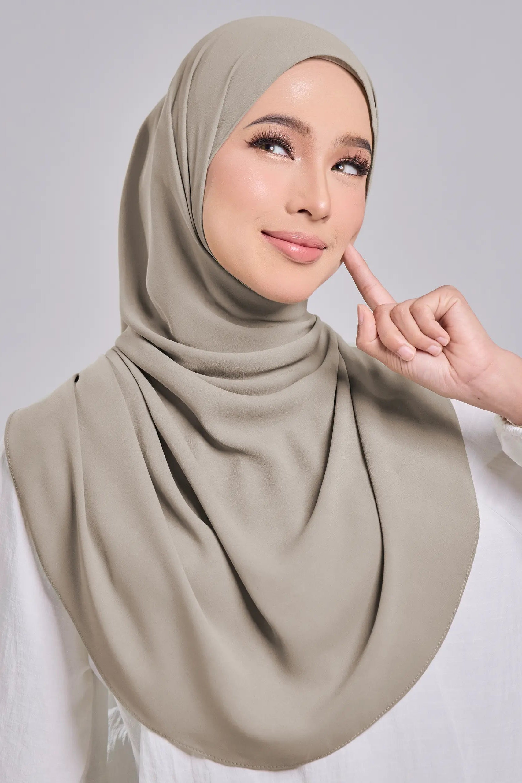 Woman wearing a beige hijab against a gray background