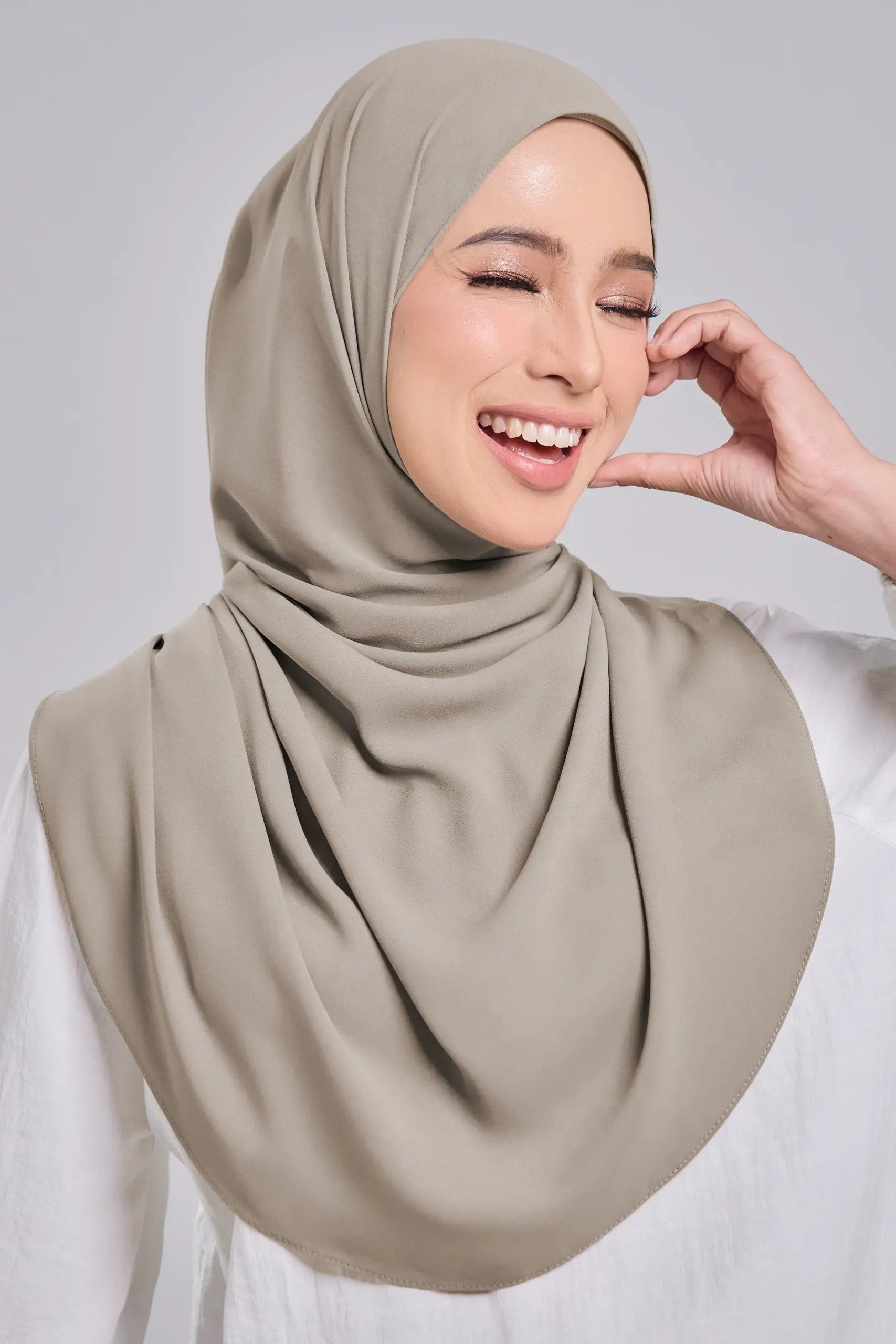 Woman wearing a beige hijab against a gray background