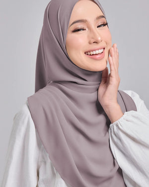 Woman wearing a light brown hijab and white top on a gray background