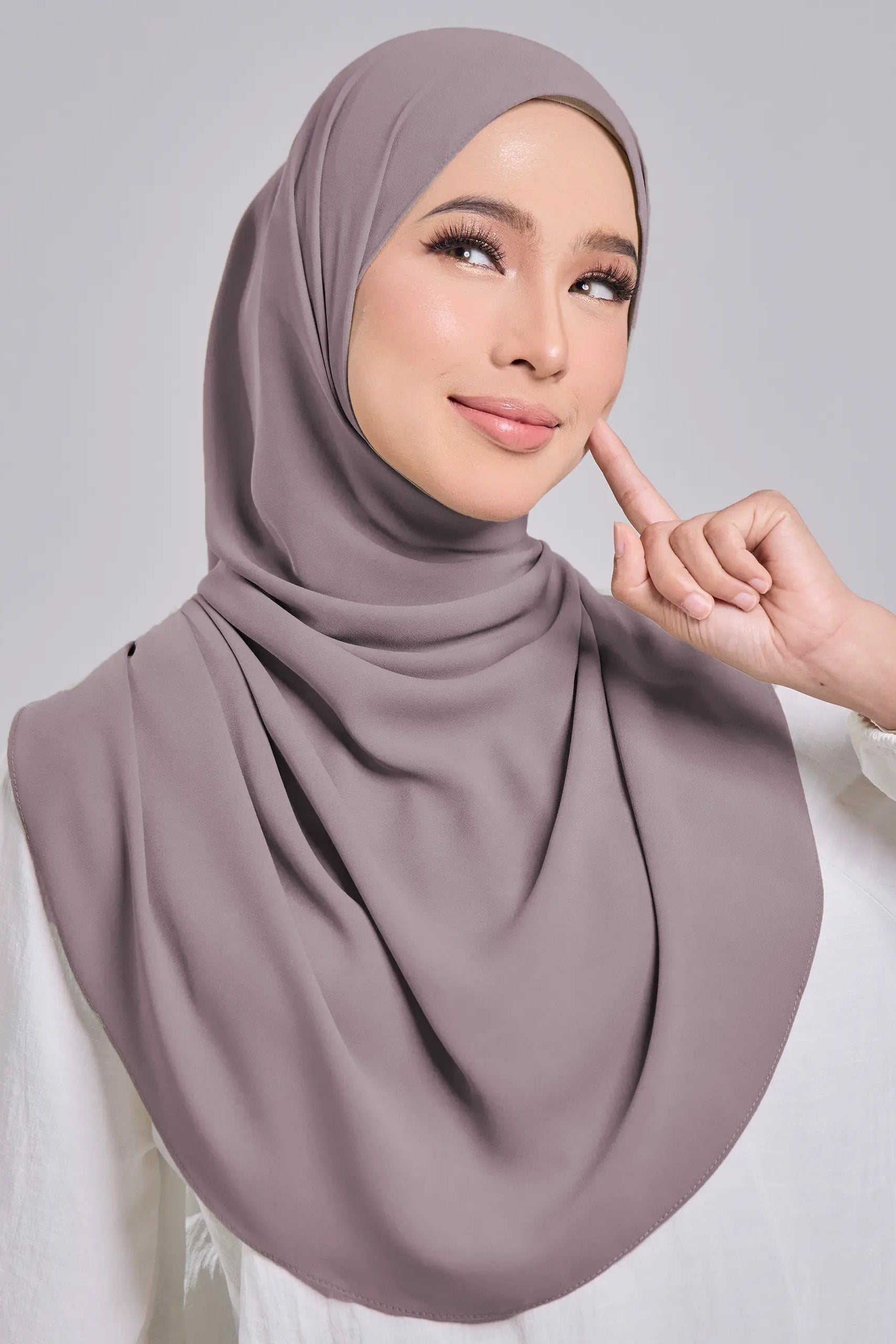 Woman wearing a gray hijab and white top on a gray background