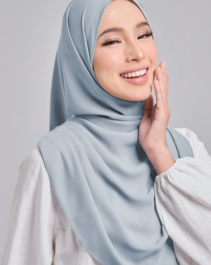Woman wearing a light blue hijab and white shirt against a gray background
