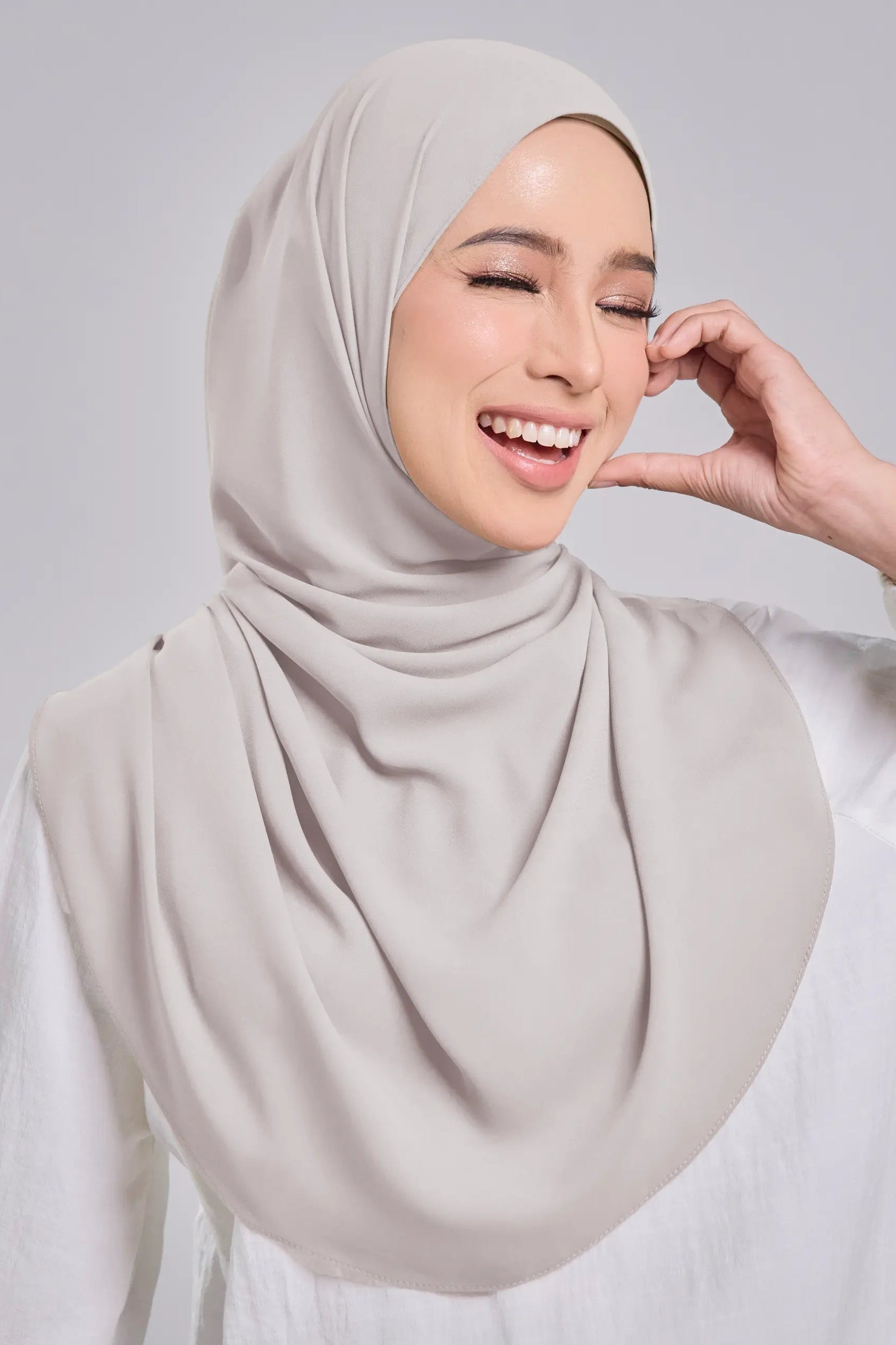Woman wearing a light gray hijab against a plain background
