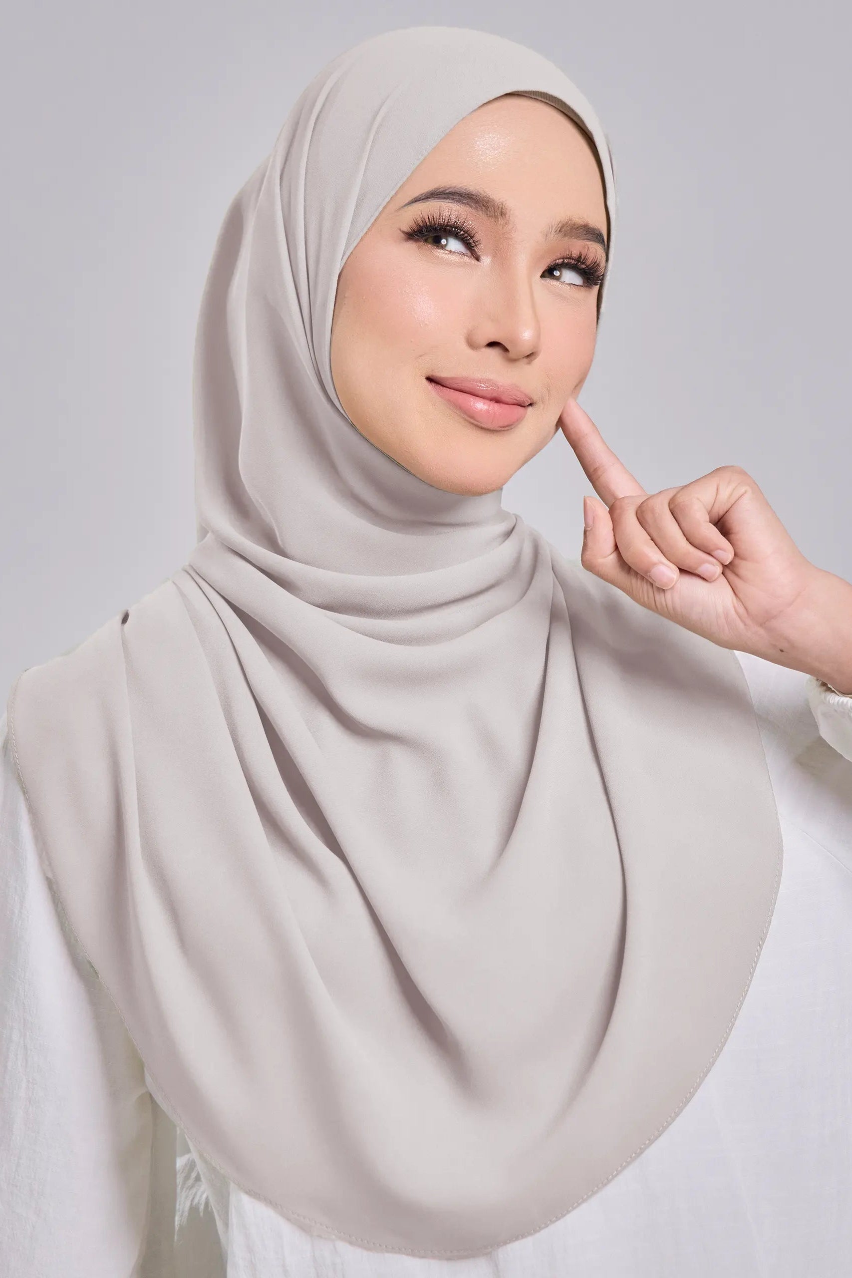 Woman wearing a light gray hijab against a plain background