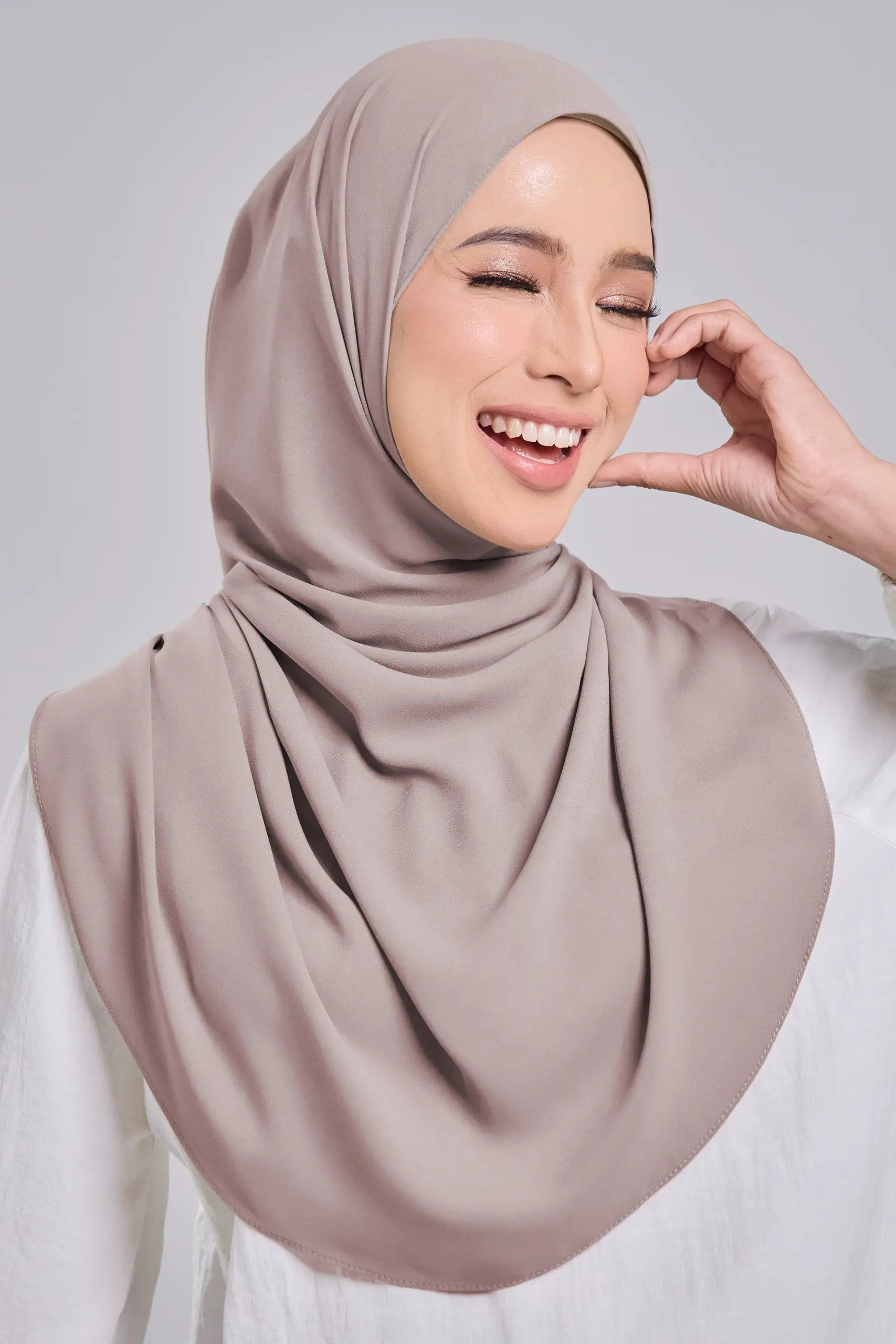 Woman wearing a beige hijab against a plain background