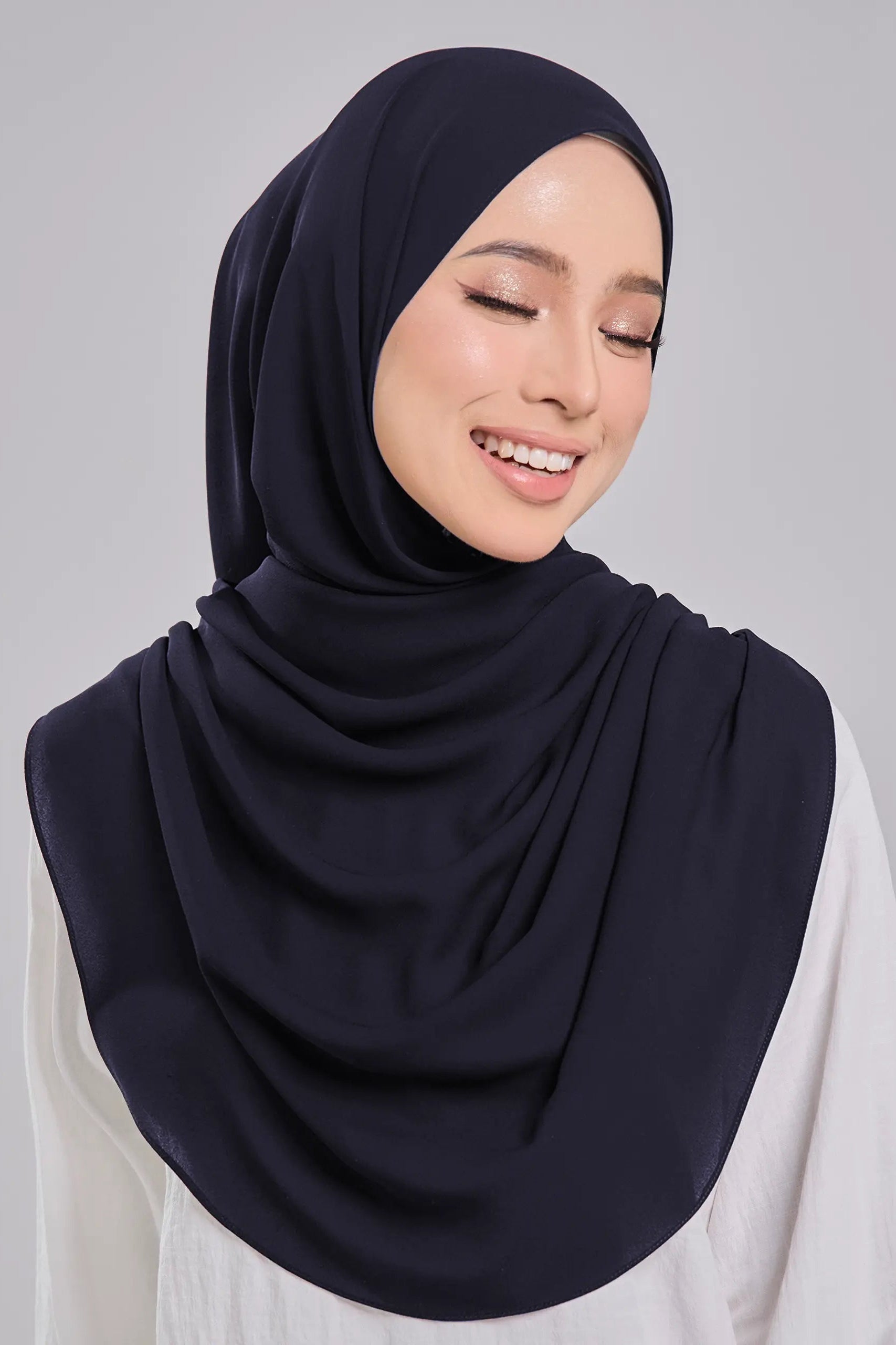 Woman wearing a navy hijab and white top on a gray background