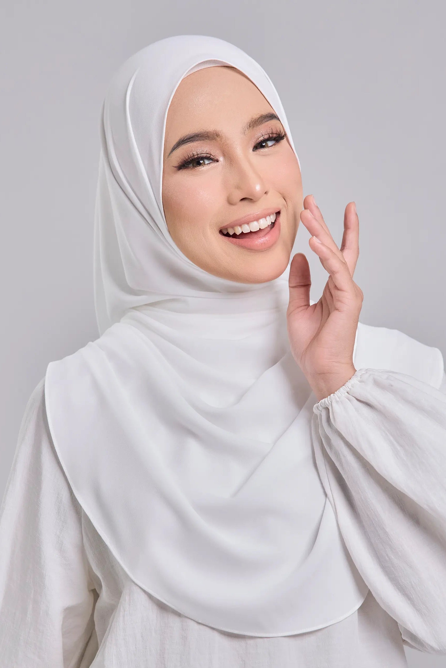 Woman wearing a white hijab and white outfit against a gray background