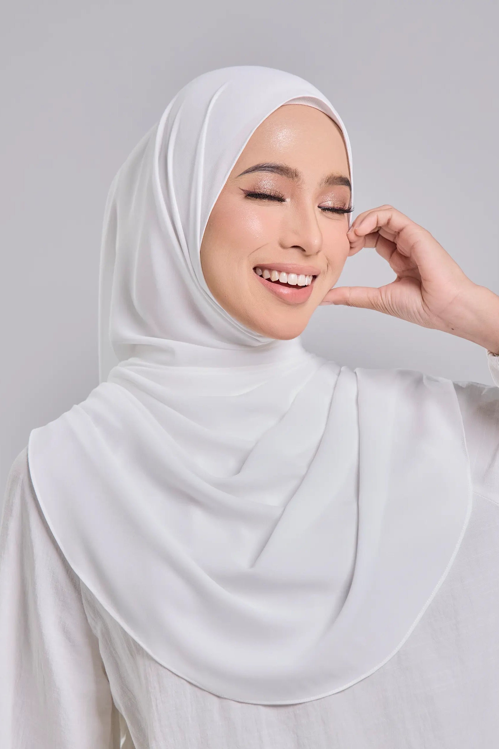 Woman wearing a white hijab against a gray background