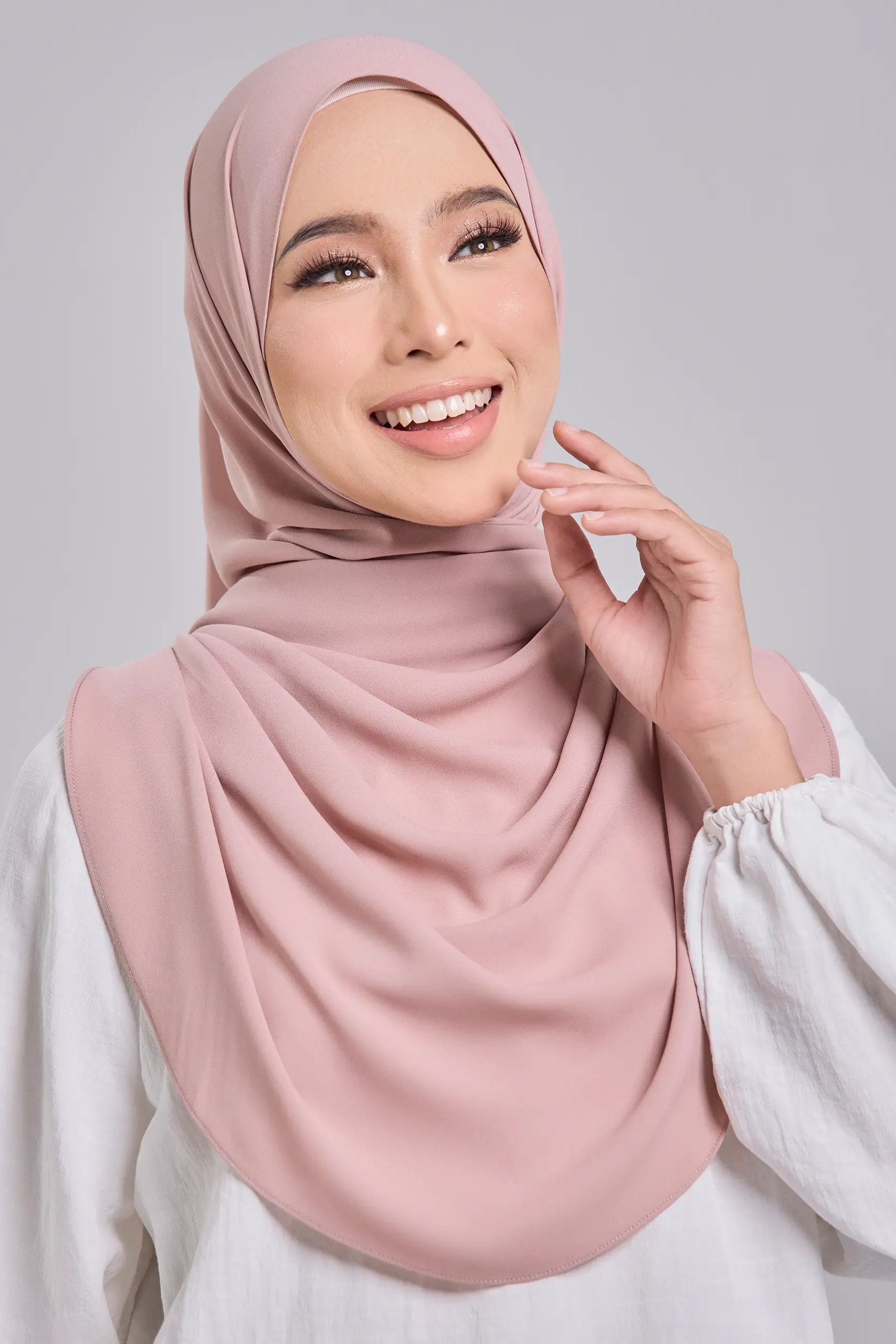 Woman wearing a pink hijab and white top against a gray background
