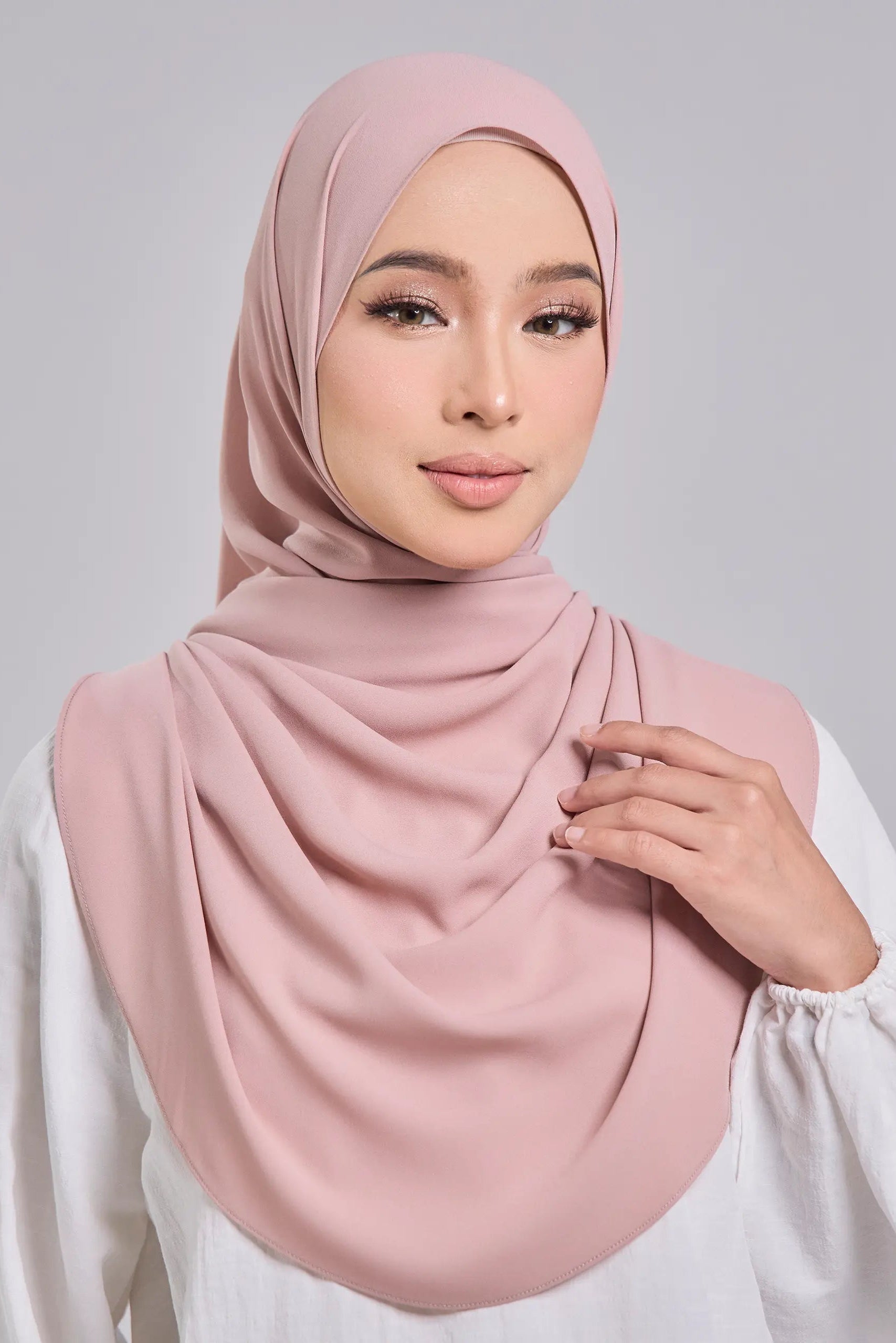 Woman wearing a pink hijab against a gray background