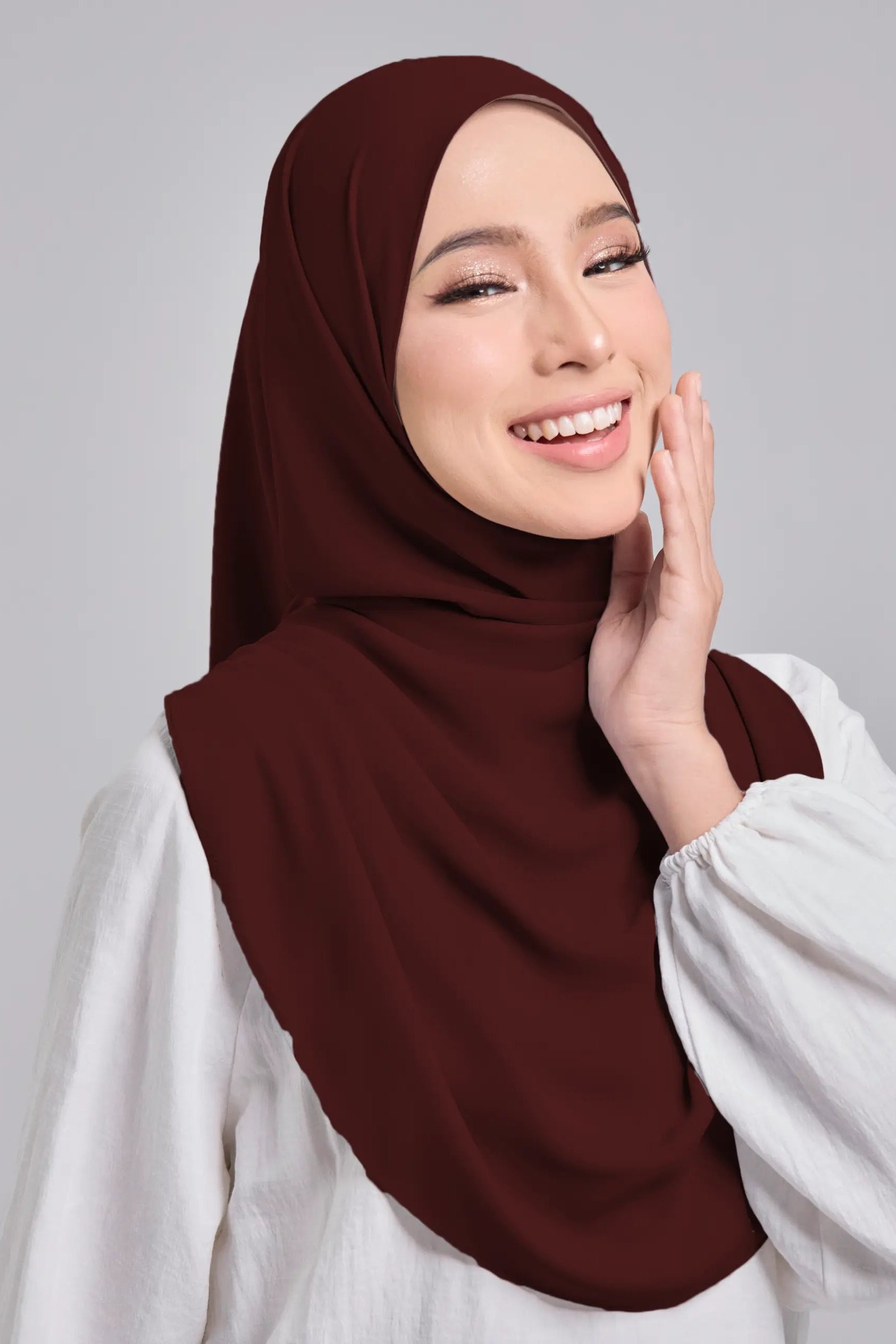 Woman wearing a brown hijab and white shirt against a gray background