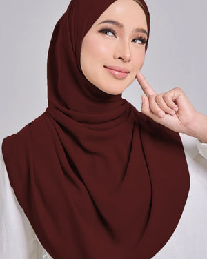 Woman wearing a brown hijab and white top on a gray background
