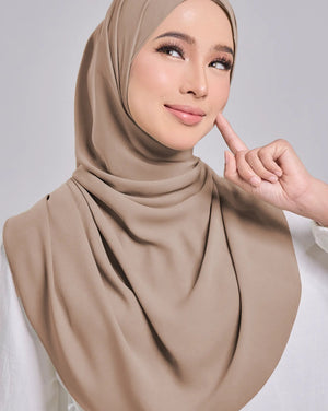 Woman wearing a beige hijab and white top on a gray background