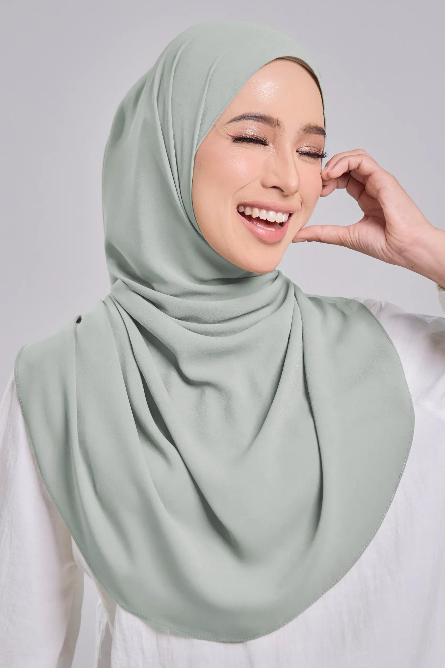 Woman wearing a light green hijab against a plain background