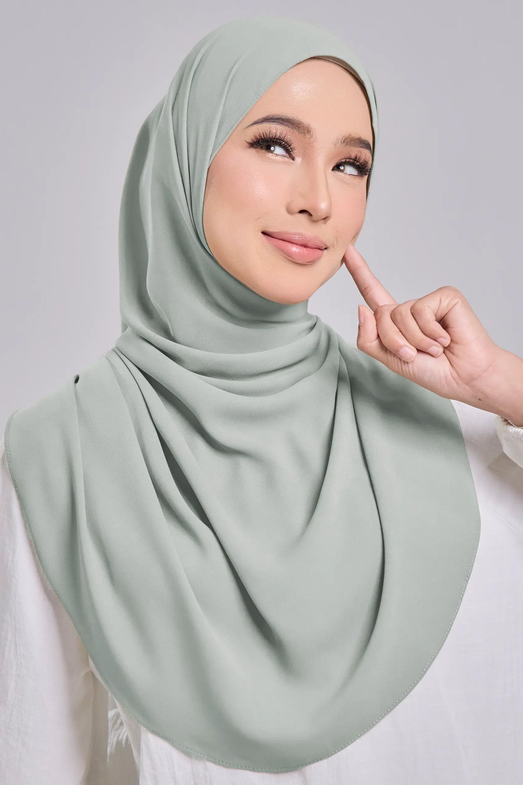 Woman wearing a light green hijab against a plain background