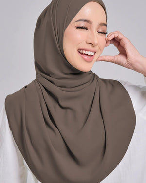 Woman wearing a brown hijab and white shirt against a gray background