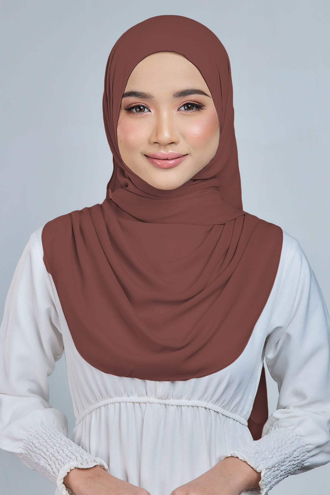 Woman wearing a brown hijab and white dress against a gray background