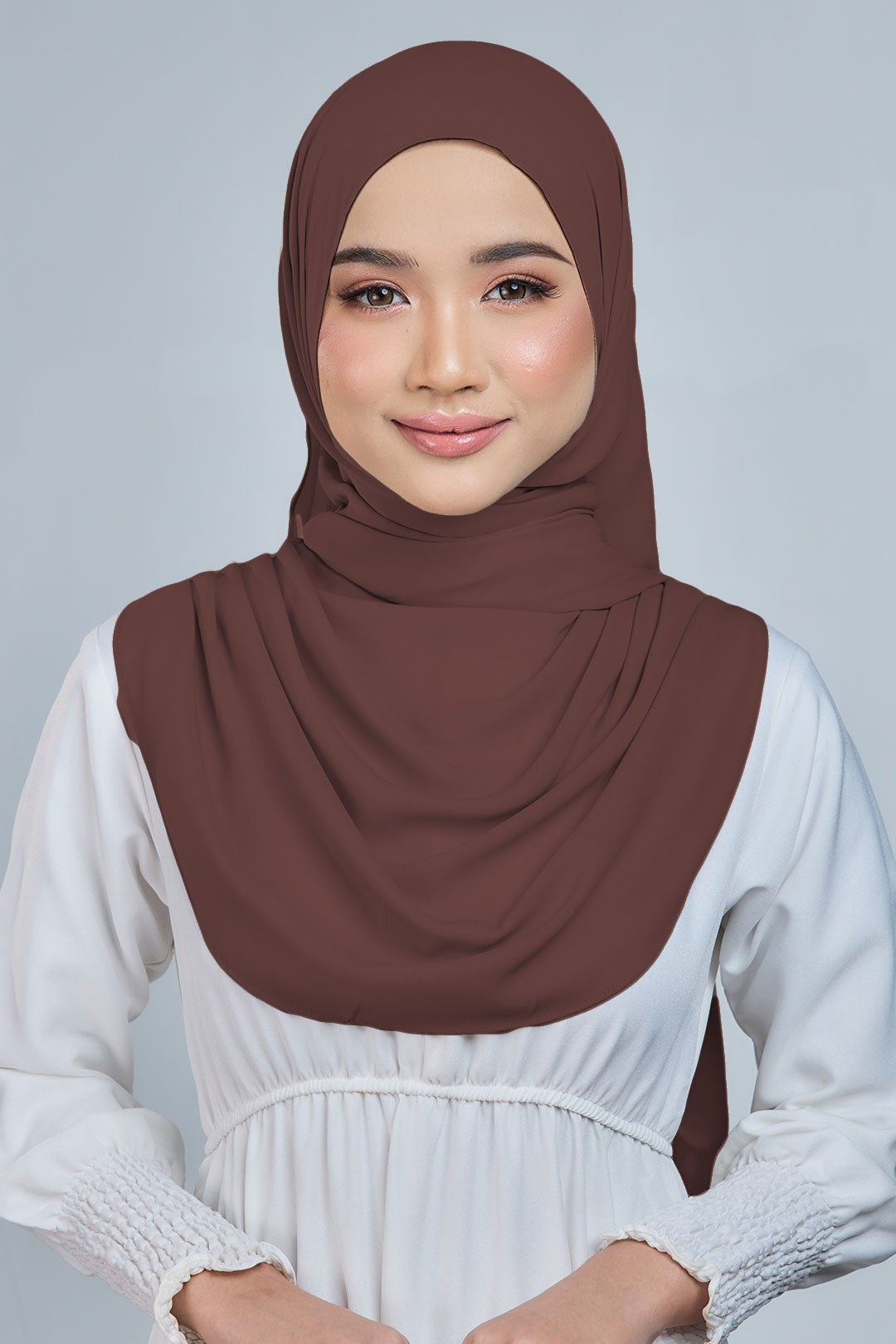 Woman wearing a brown hijab and white dress against a gray background