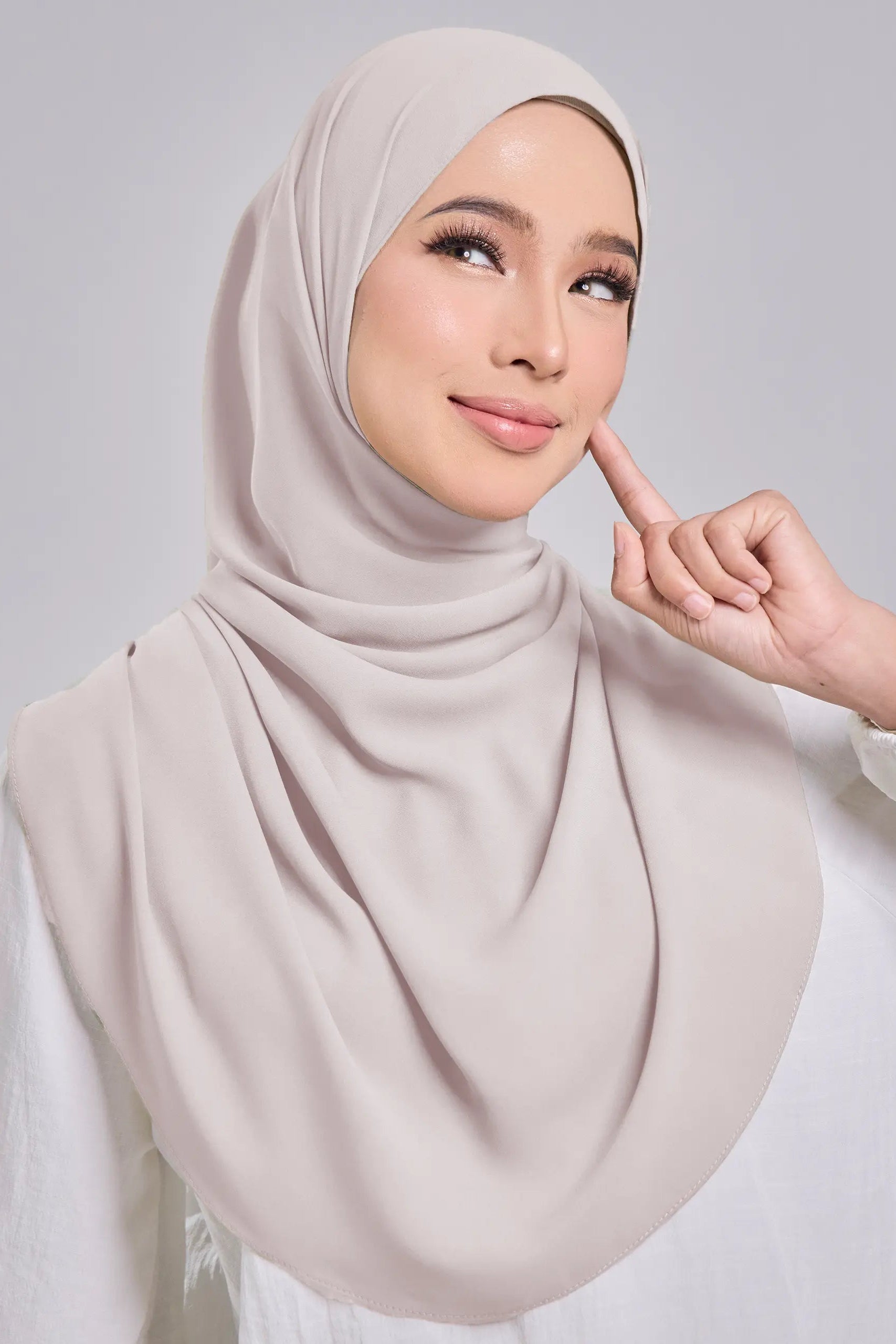 Woman wearing a beige hijab against a gray background