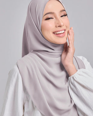 Woman wearing a light gray hijab and white top against a plain background