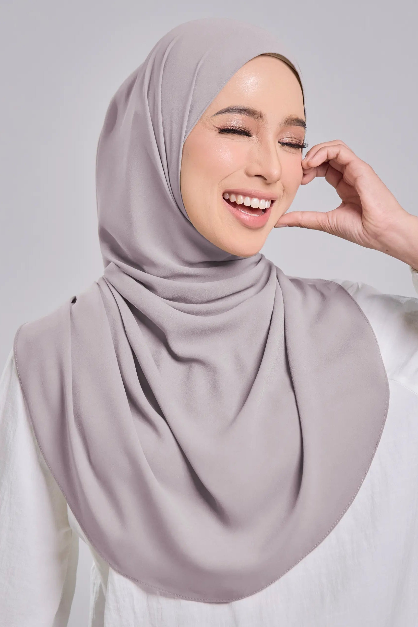 Woman wearing a light gray hijab against a plain background