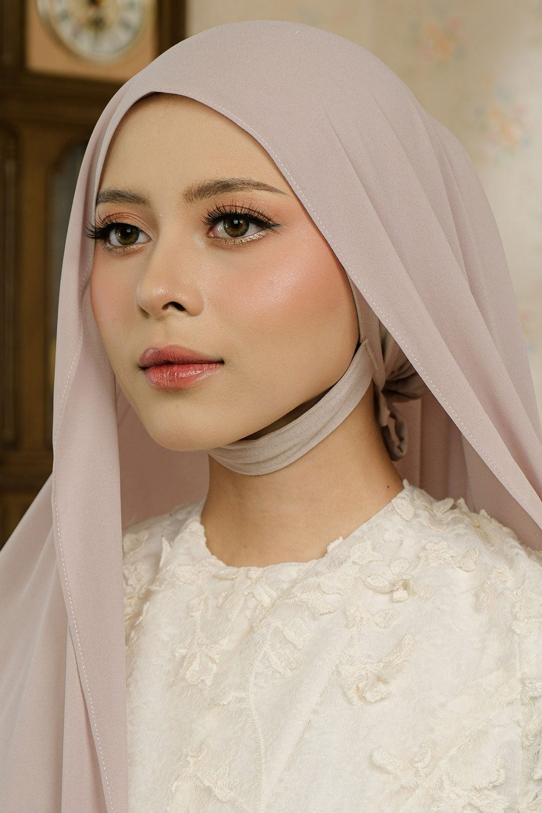 Woman wearing a light pink hijab and white floral dress indoors.
