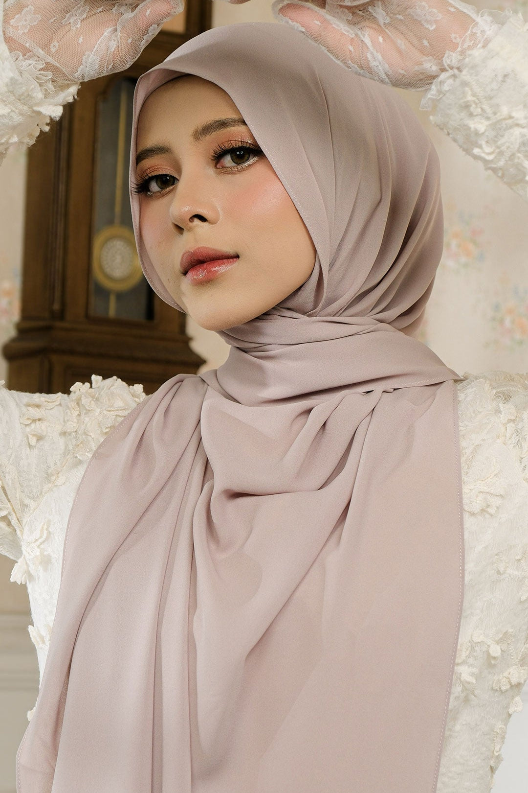 Woman wearing a beige hijab with lace gloves in a decorative setting