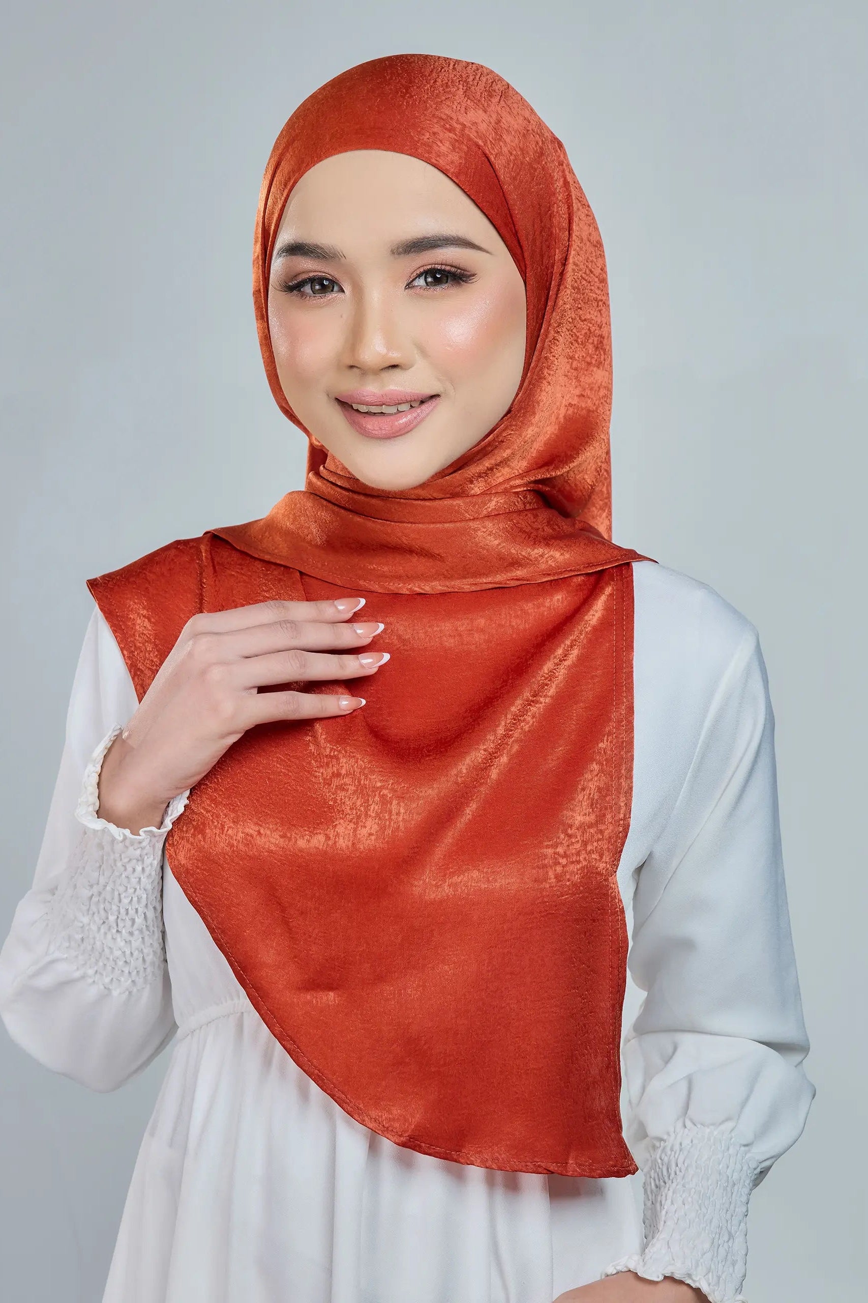 Woman wearing an orange hijab and white top on a gray background
