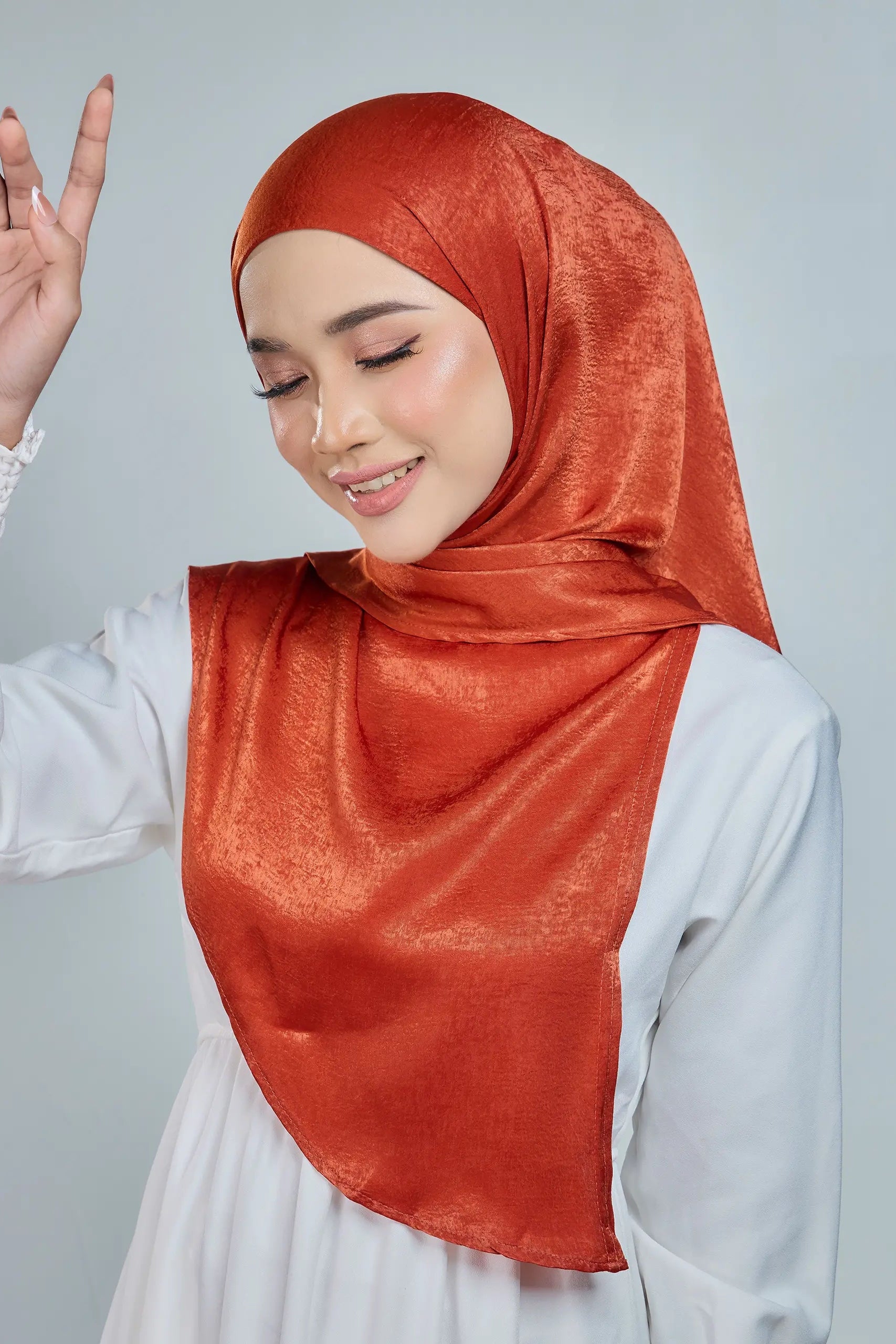 Woman wearing a rust-colored hijab and white outfit on a light gray background