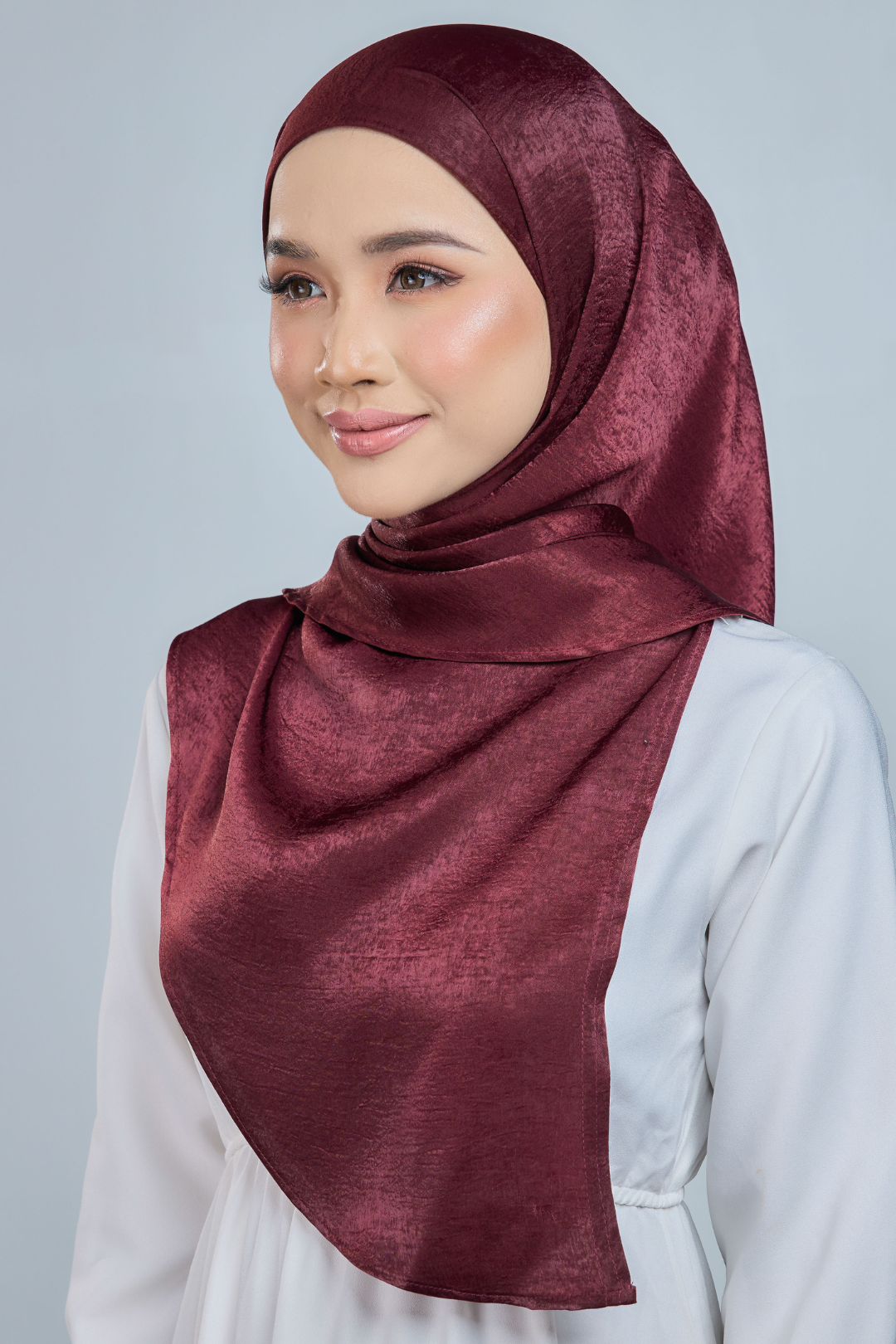 A person wearing a red half moon shaped shawl made of velvet satin with an adjustable tie back band.