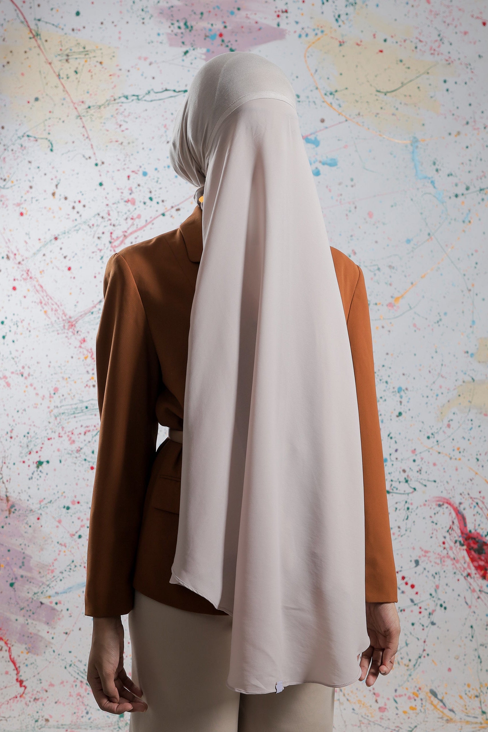 Person wearing a brown blazer and beige hijab against a colorful abstract background