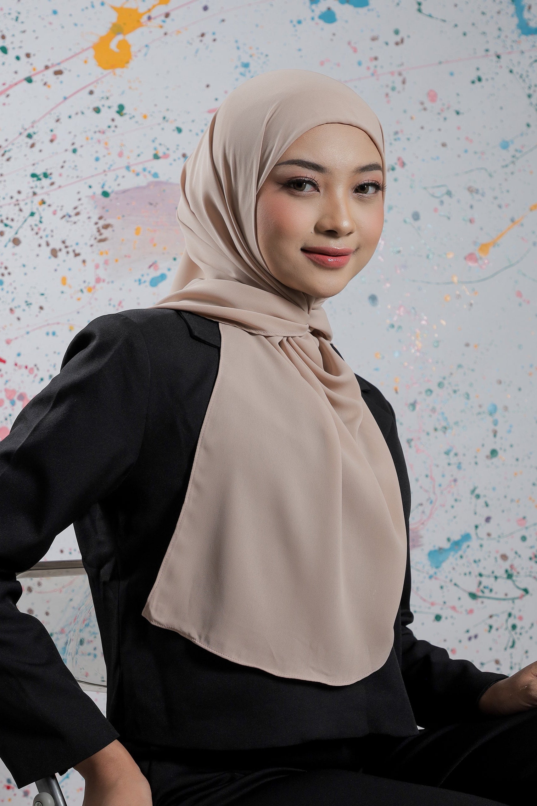 Woman wearing a beige hijab against a colorful abstract background