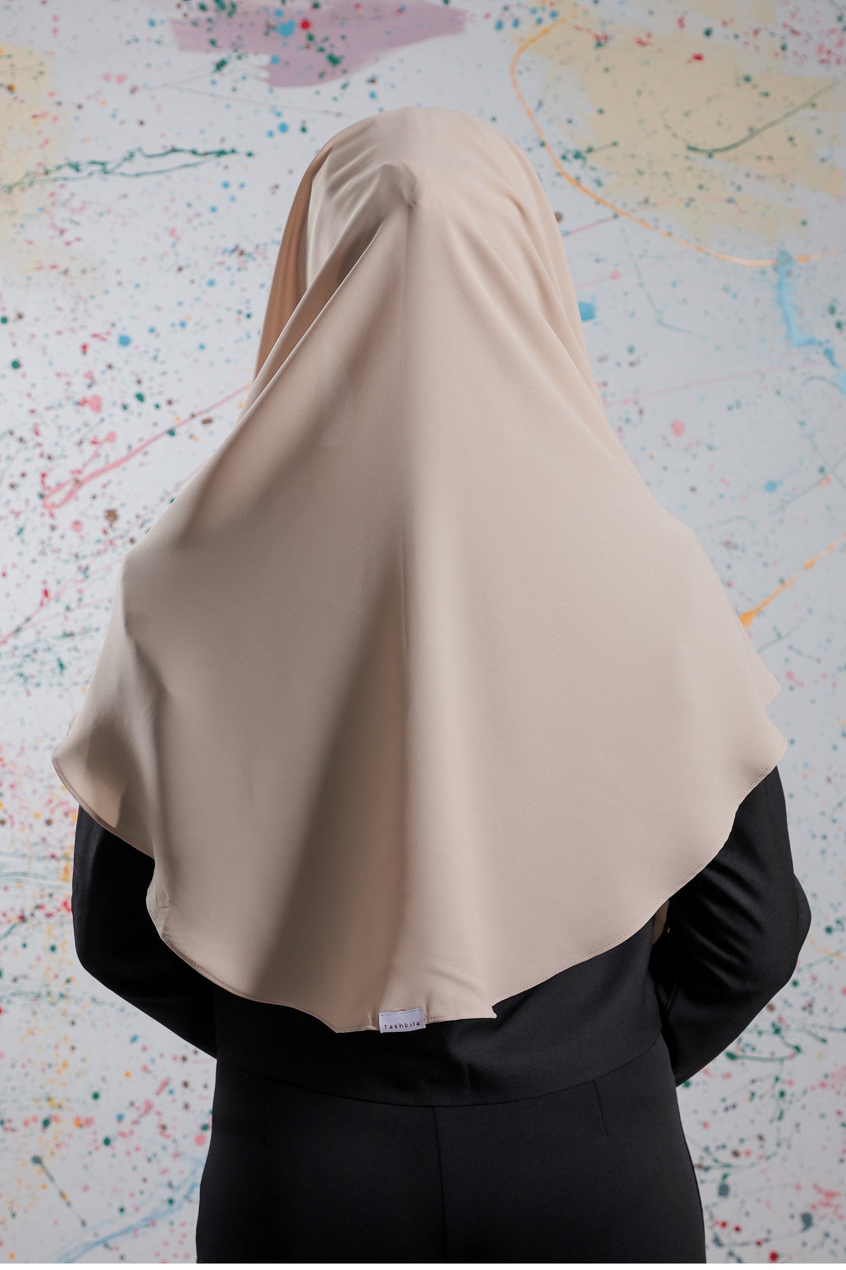 Person wearing a beige hijab against a colorful abstract background