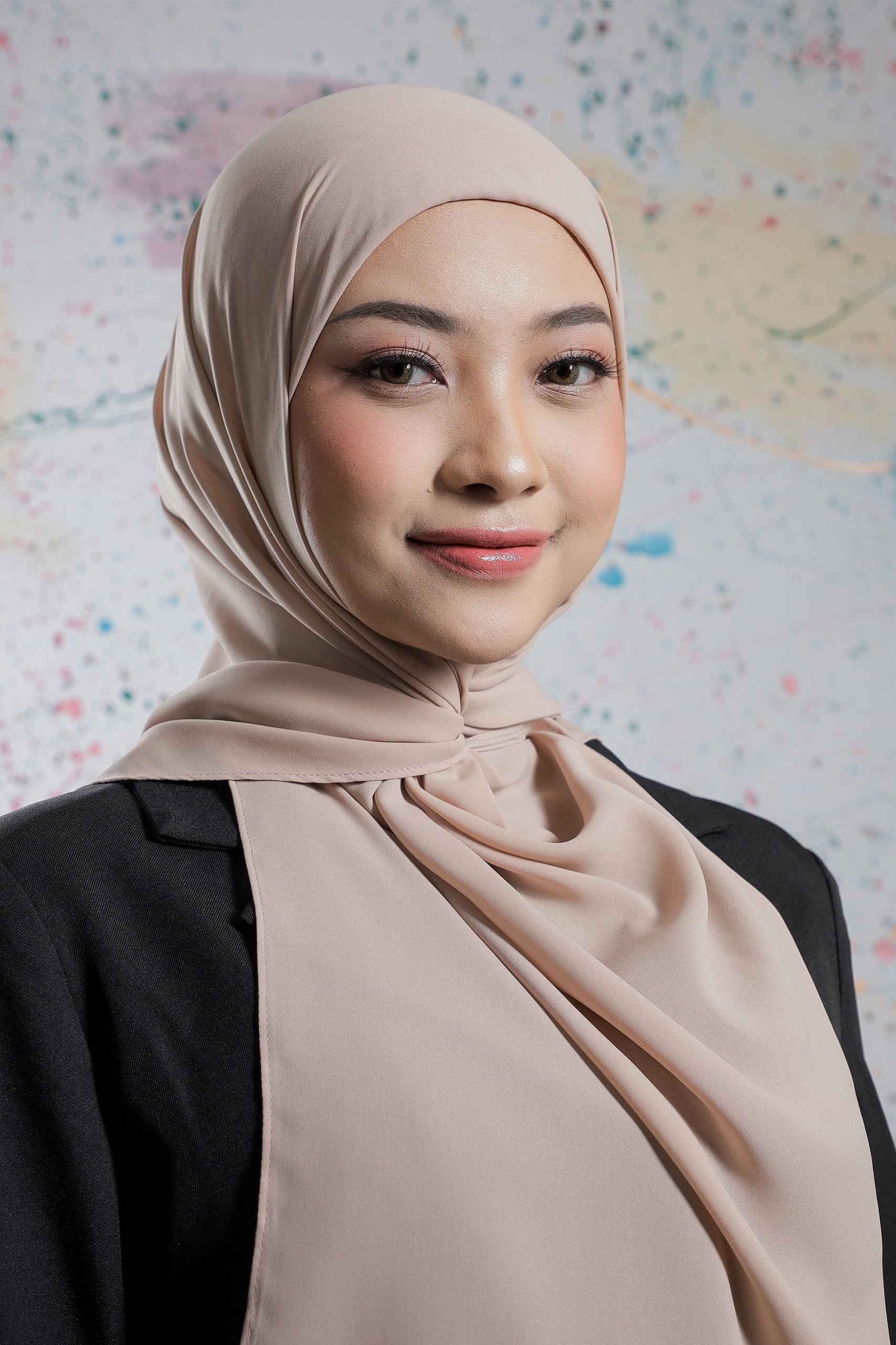 Woman wearing a beige hijab against a colorful abstract background