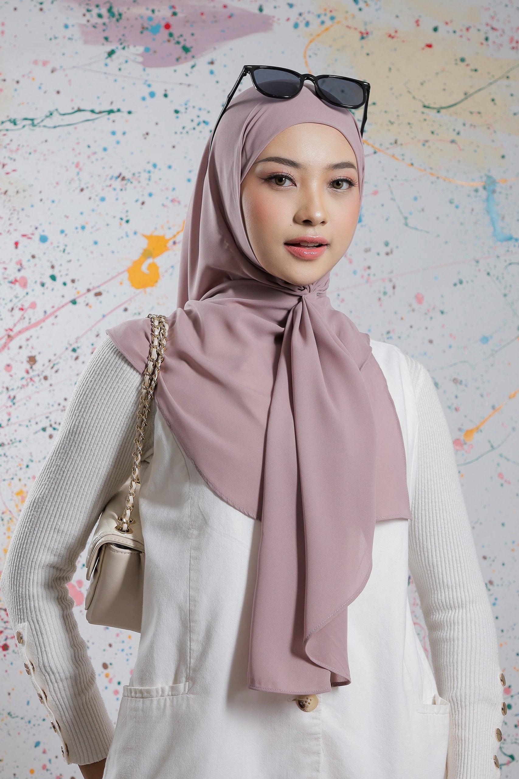 Woman wearing a pink hijab and sunglasses on a colorful abstract background