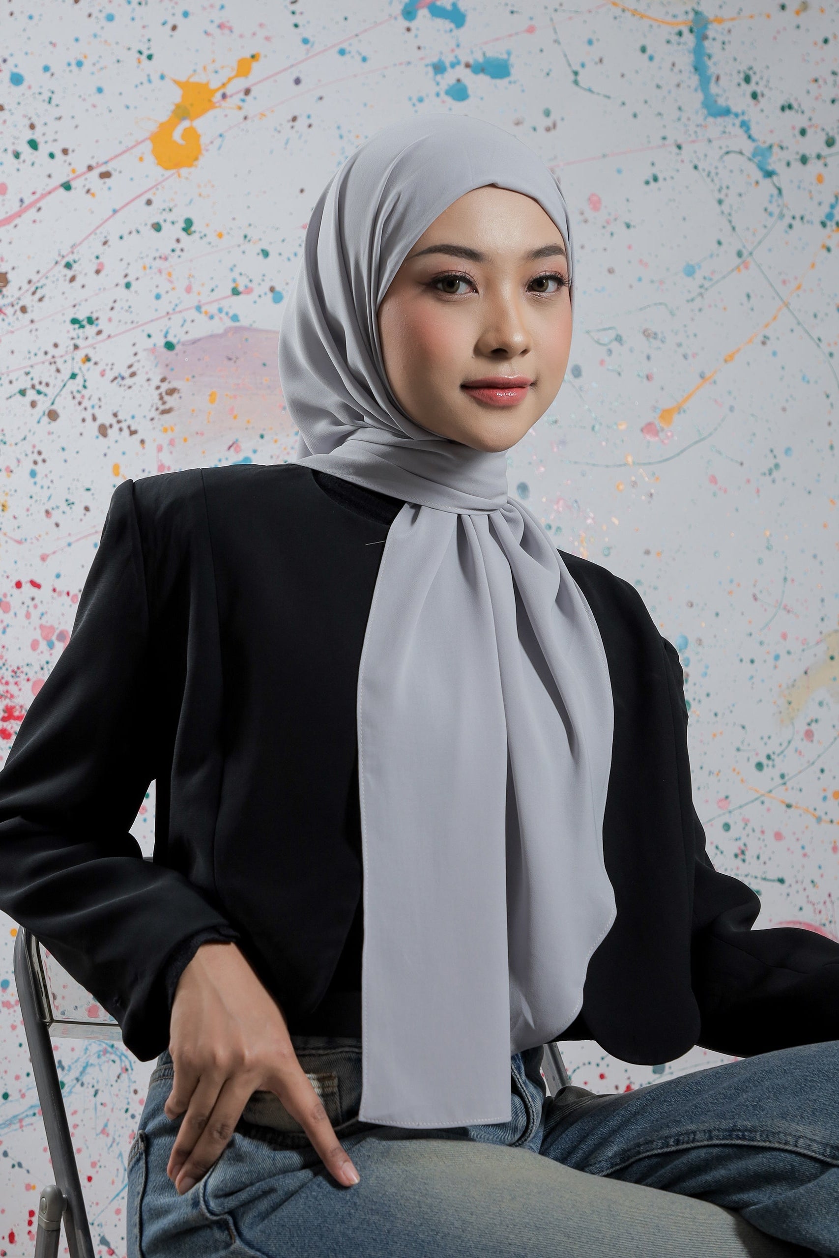 Woman wearing a hijab sitting against a colorful abstract background