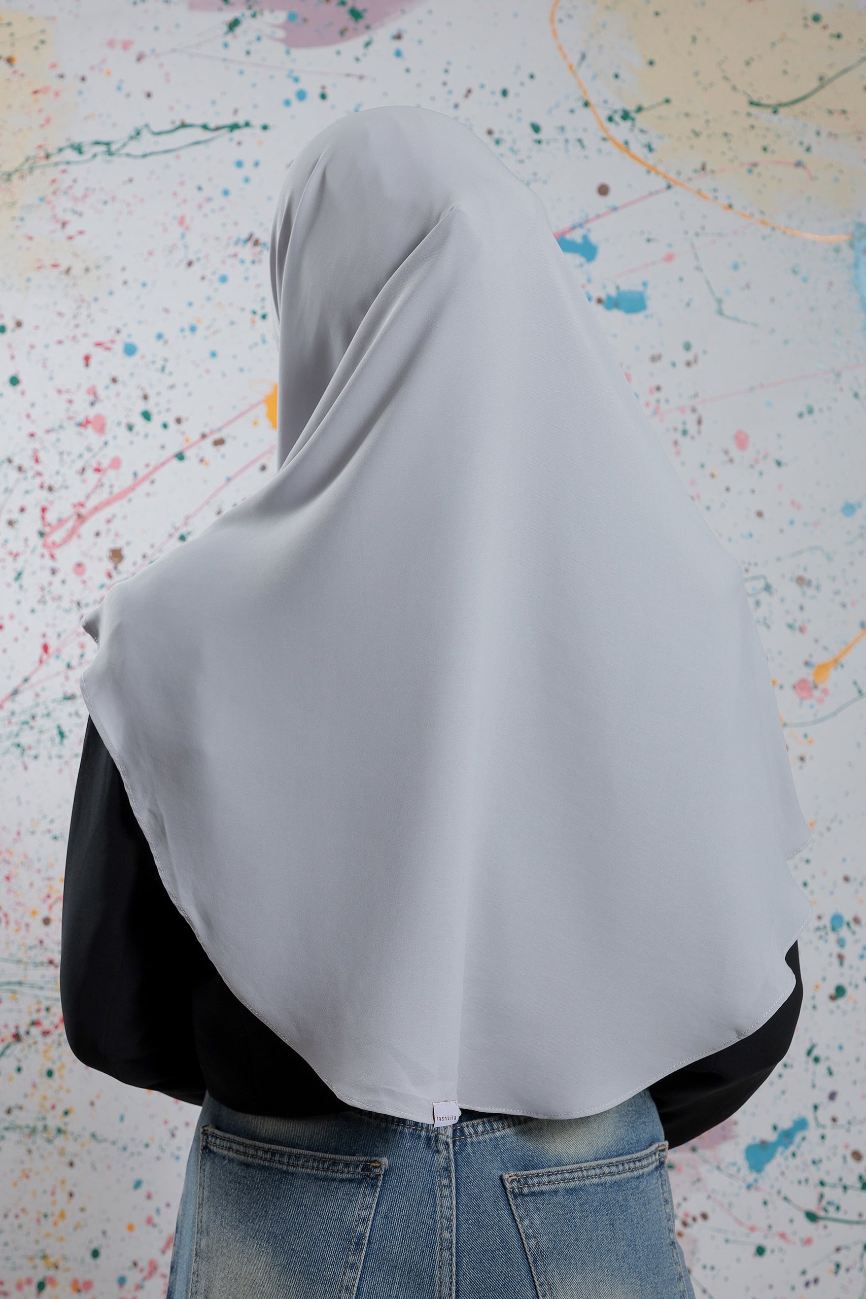 Person wearing a gray hijab with a colorful abstract pattern in the background