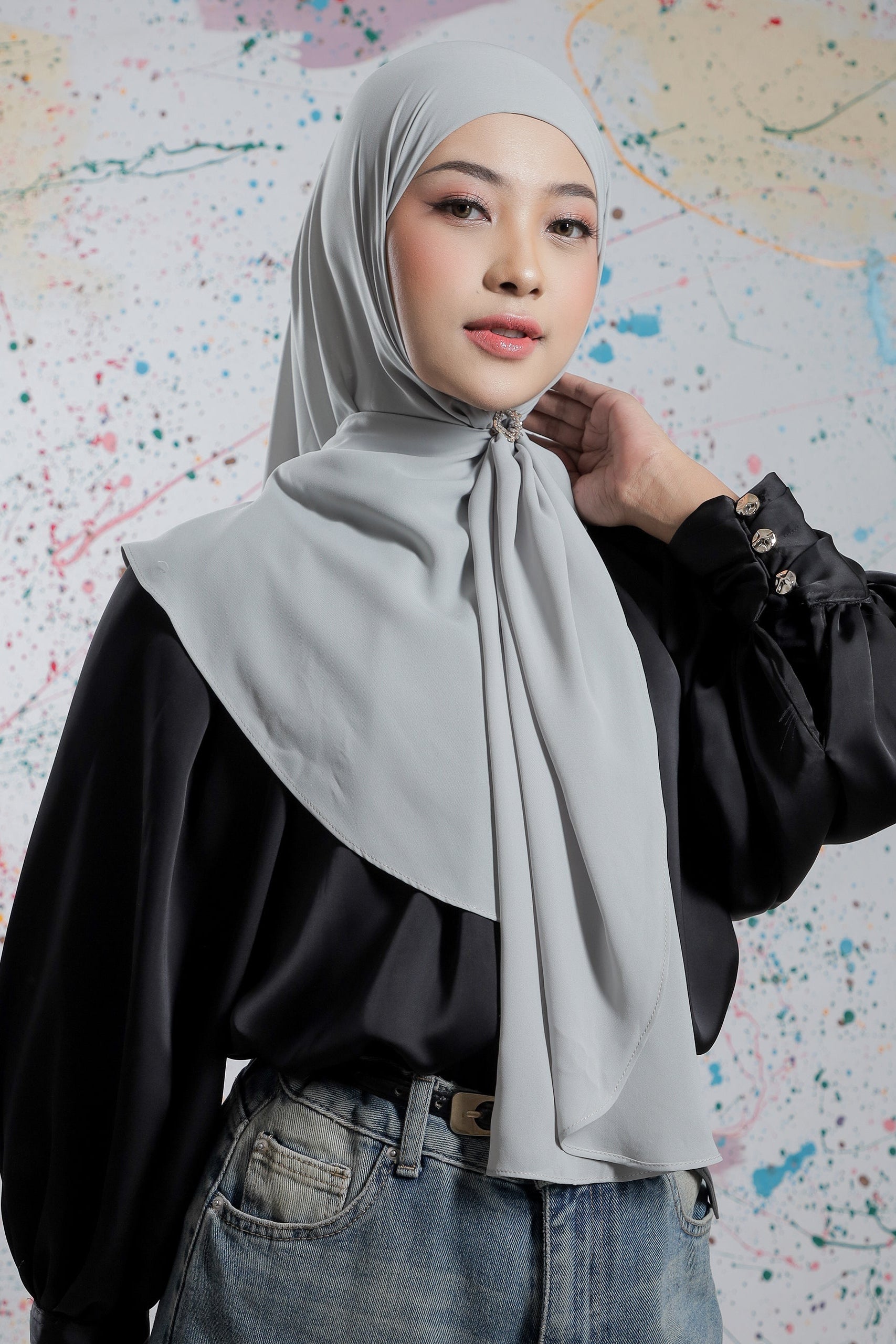 Woman wearing a gray hijab and black top against a colorful abstract background