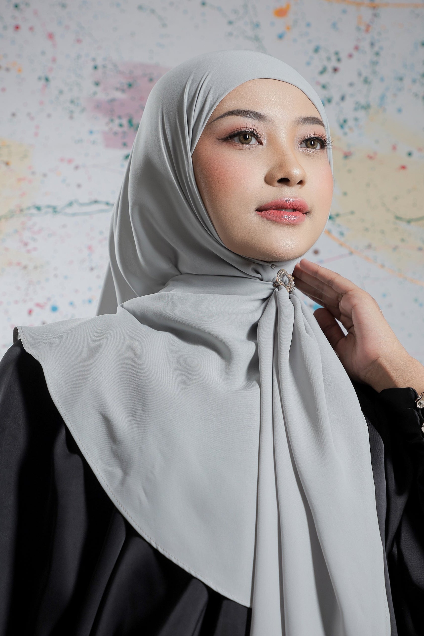 Woman wearing a light gray hijab against a colorful abstract background