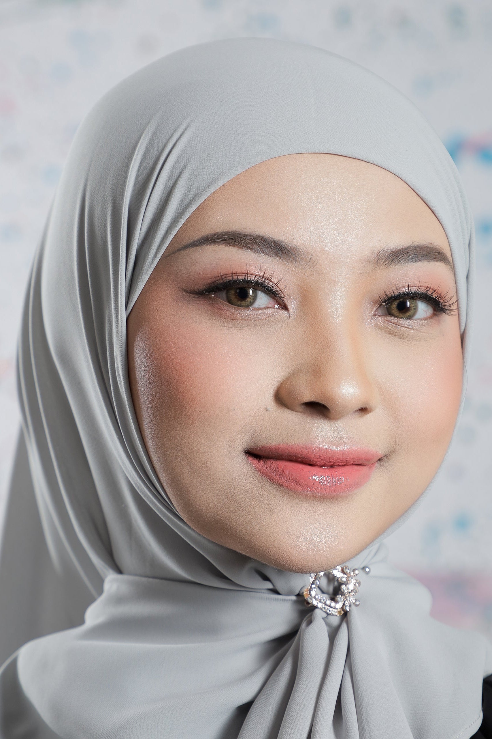 Woman wearing a gray hijab with a decorative bow against a light background