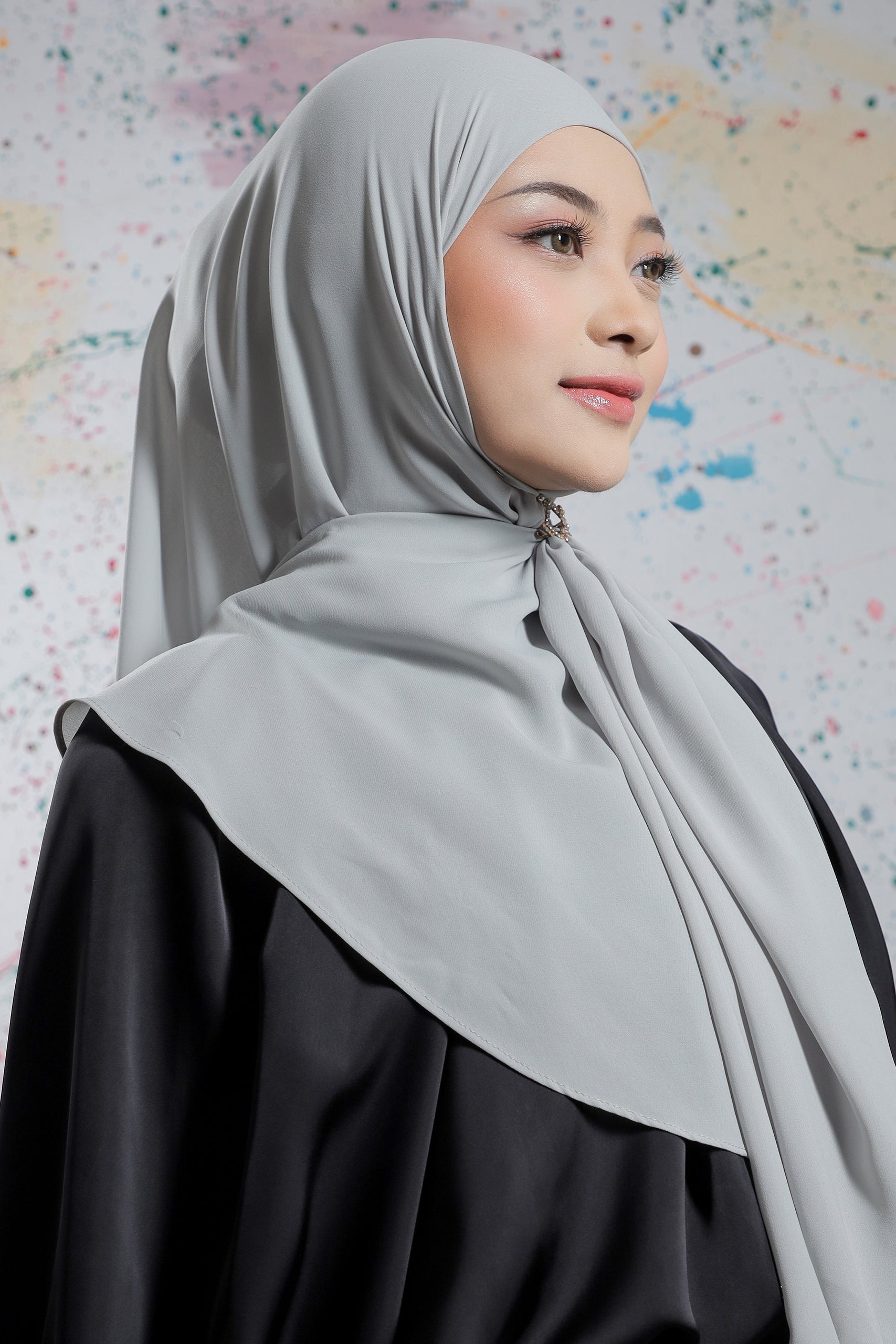 Woman wearing a light gray hijab and black clothing against a colorful abstract background