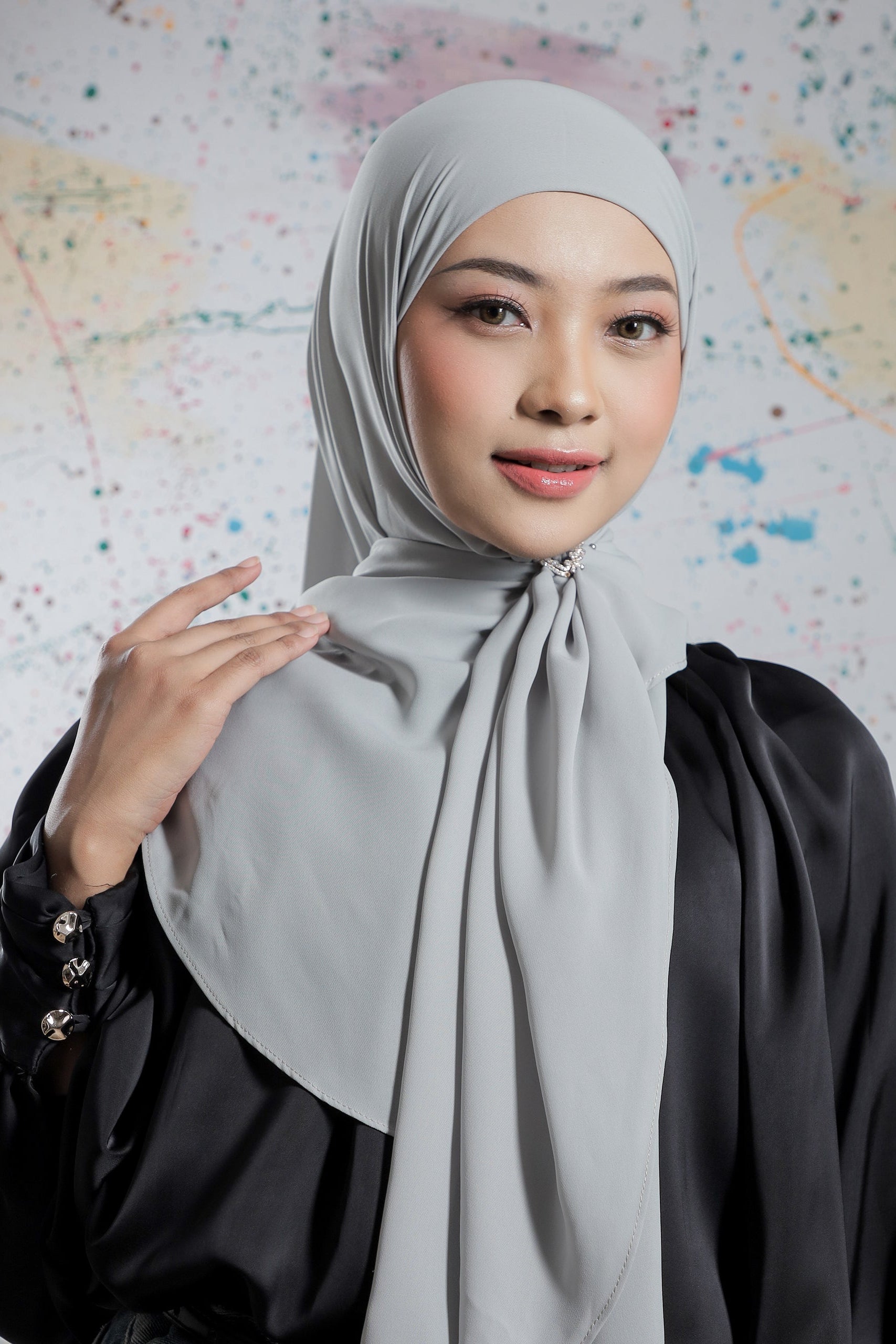 Woman wearing a light gray hijab against a colorful abstract background