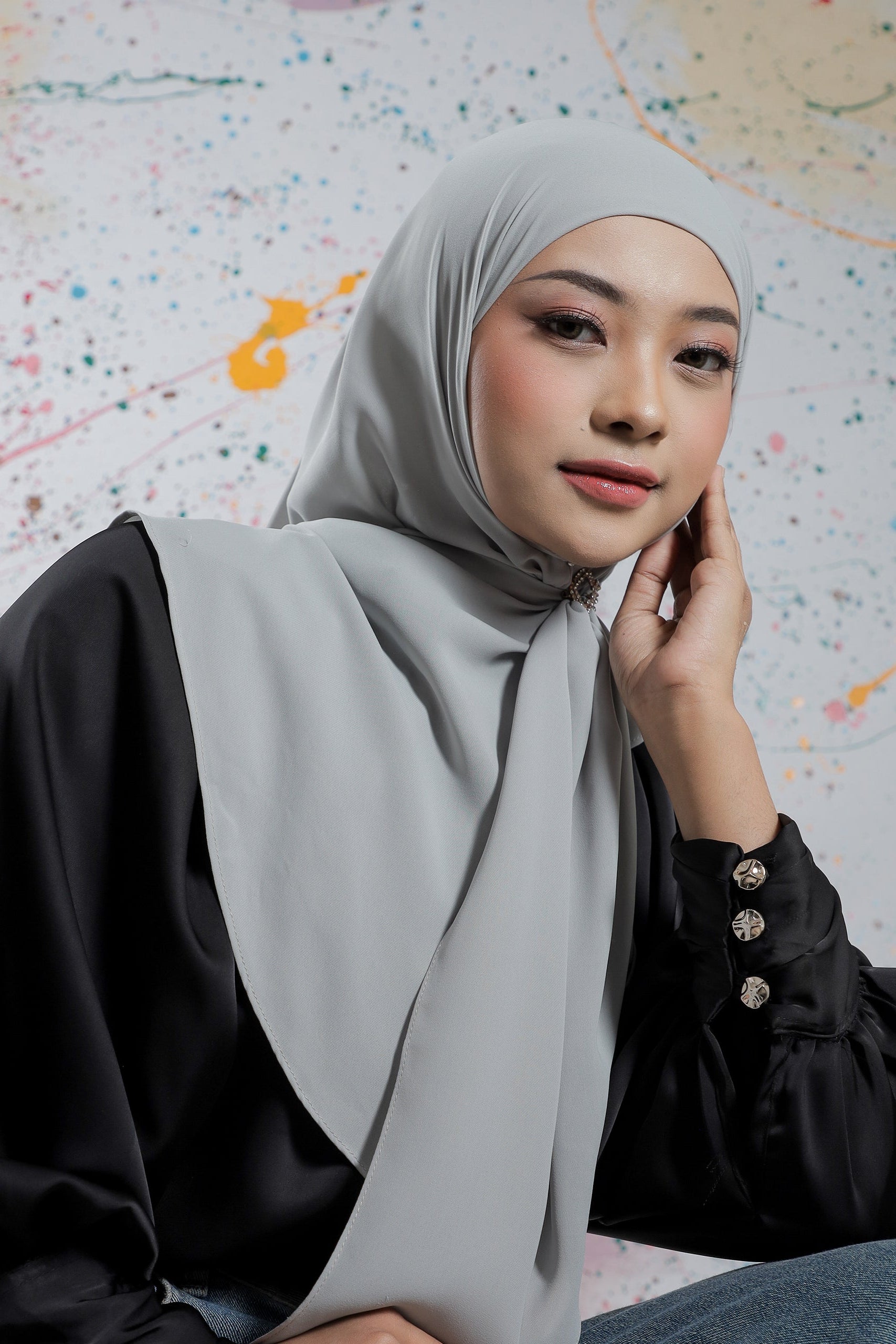Woman wearing a light gray hijab and black outfit against a colorful abstract background