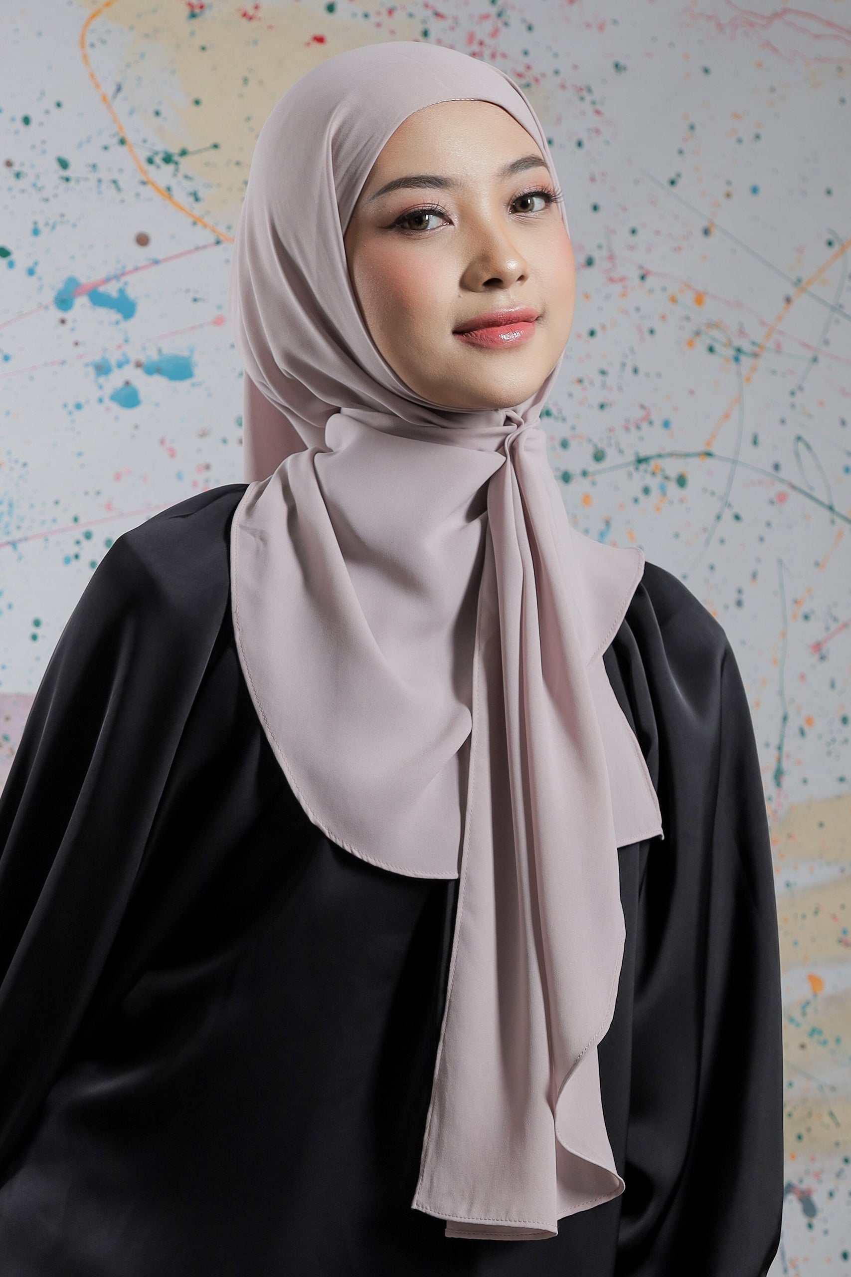 Woman wearing a light pink hijab and black outfit against a colorful abstract background